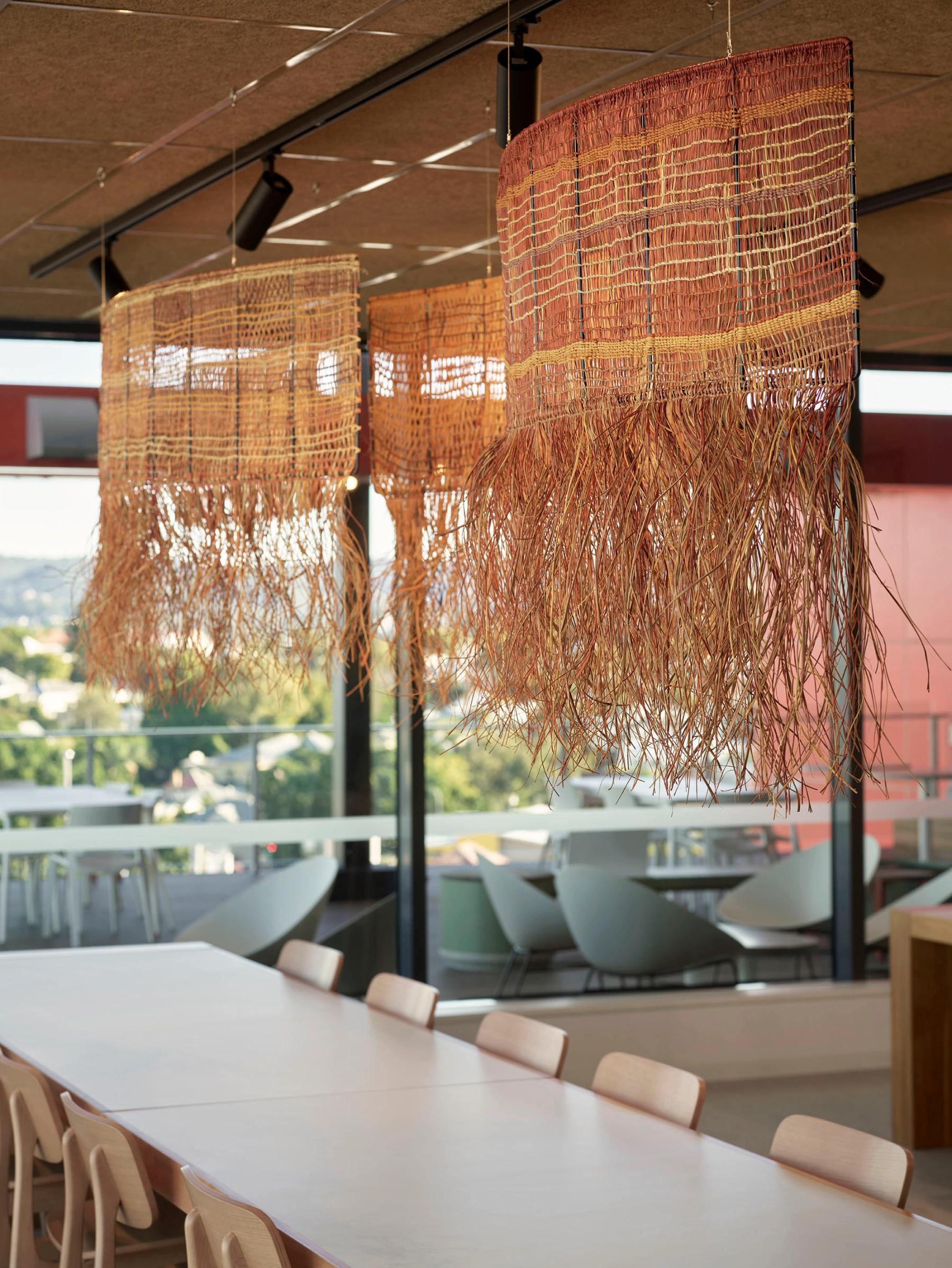 Close up of woven pendants hanging above long table with chairs. 