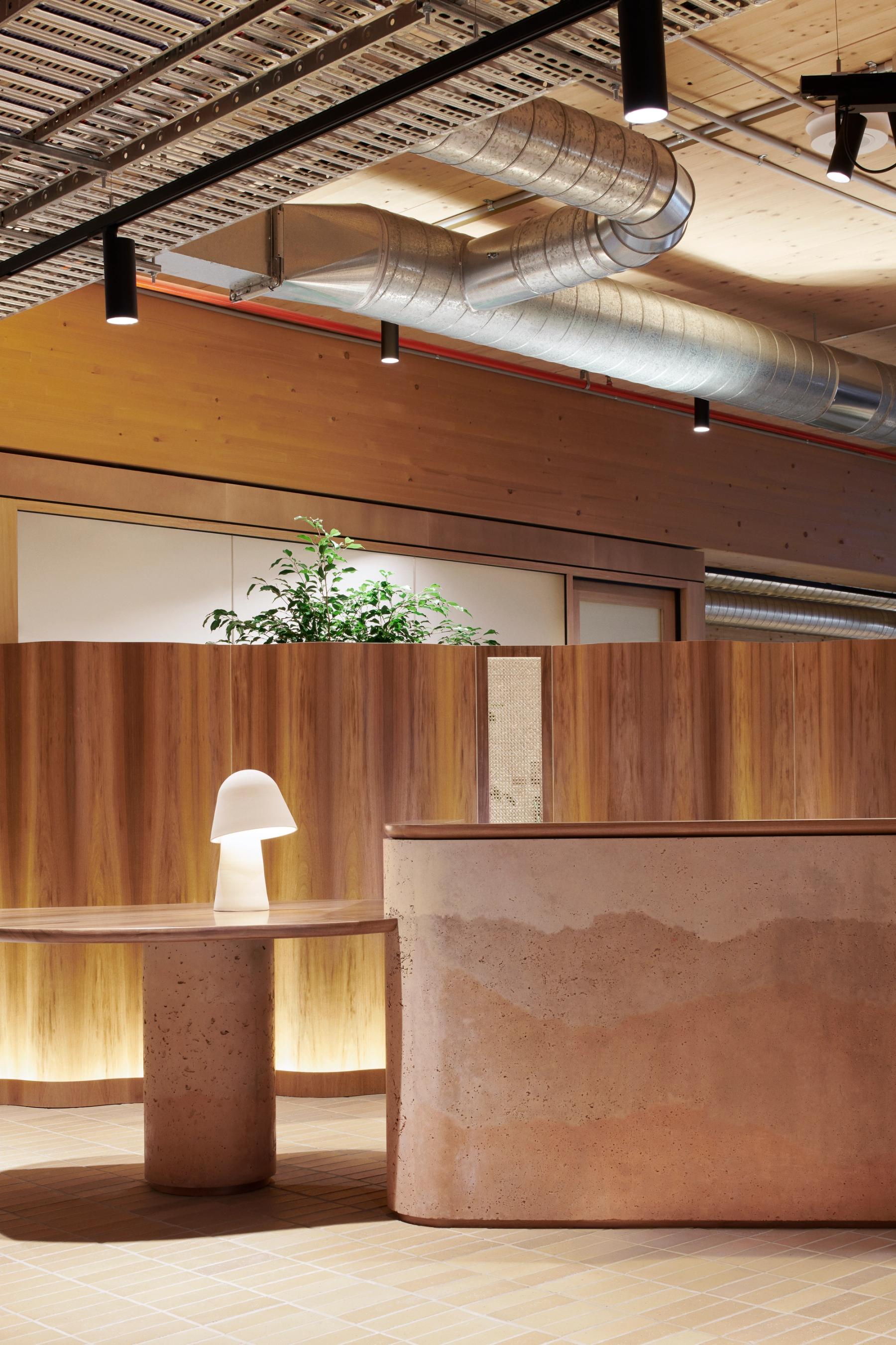 Office reception area with a curved desk, wooden table, white lamp, wooden panelling and an indoor plant.