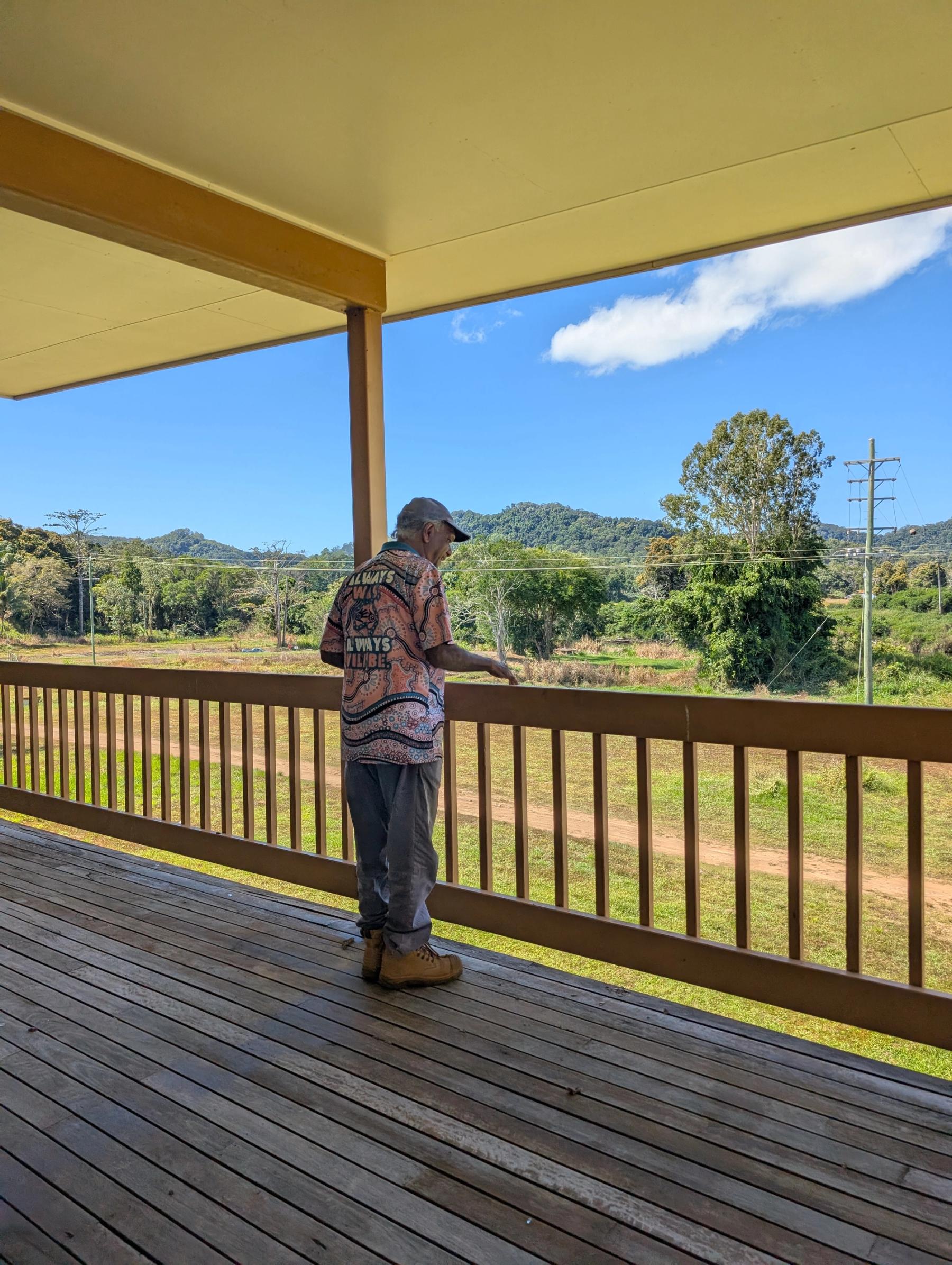 Man standing on a wooden porch looking out onto a green landscape.