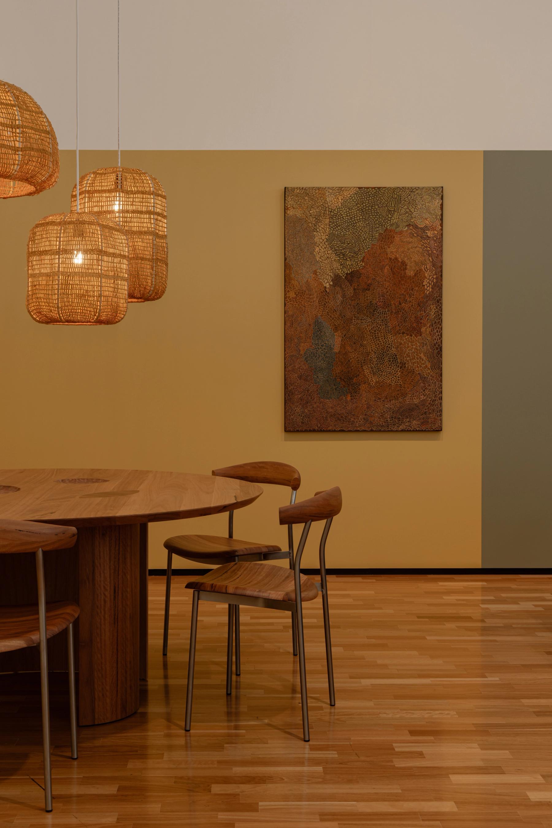 Dining space with wooden dining table and chairs, three woven pendant lights and artwork on the wall.