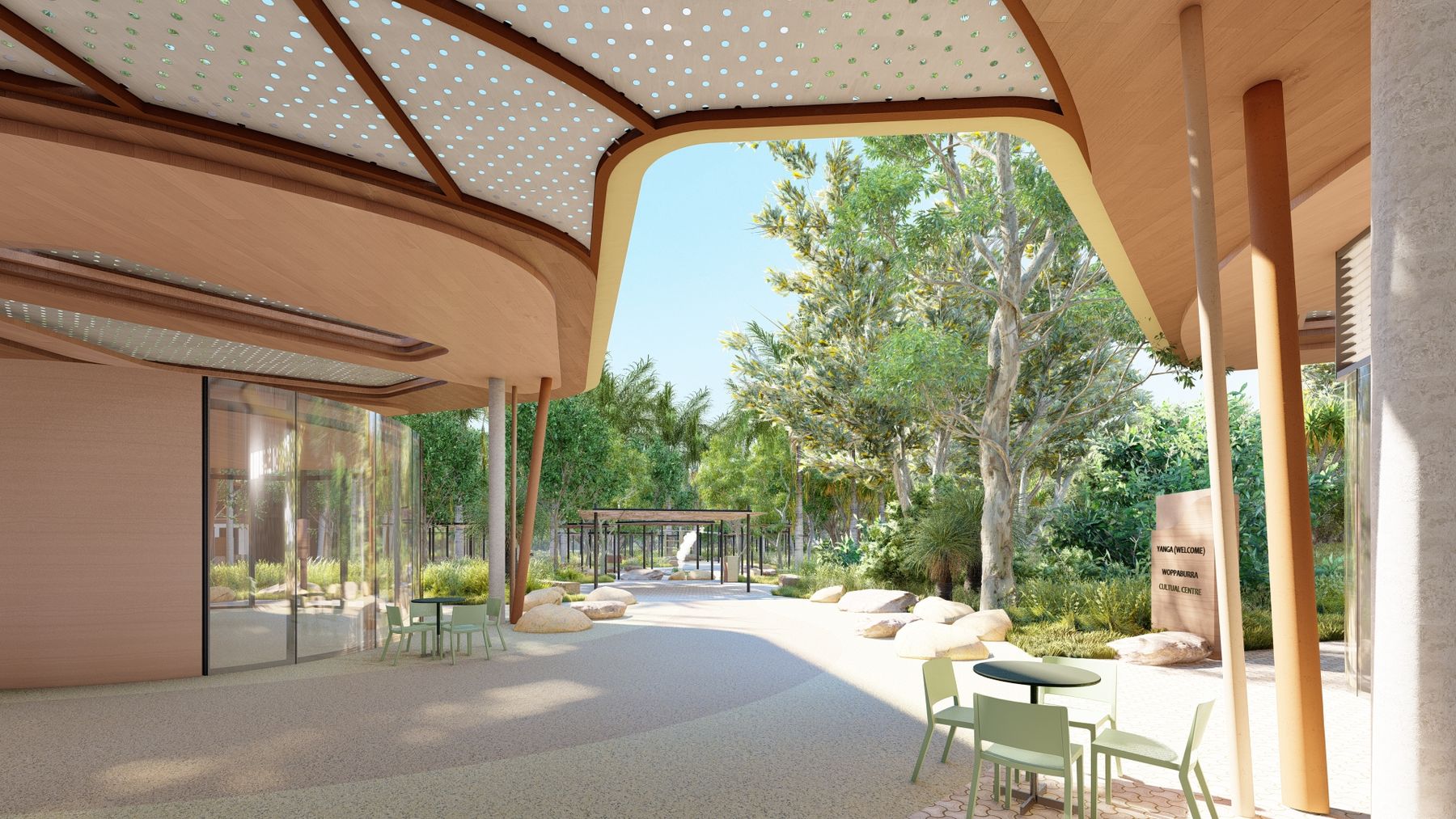 Shaded courtyard with curved timber canopy featuring circular cutouts, green tables and seating, gardens and sign for Woppaburra Cultural Centre.