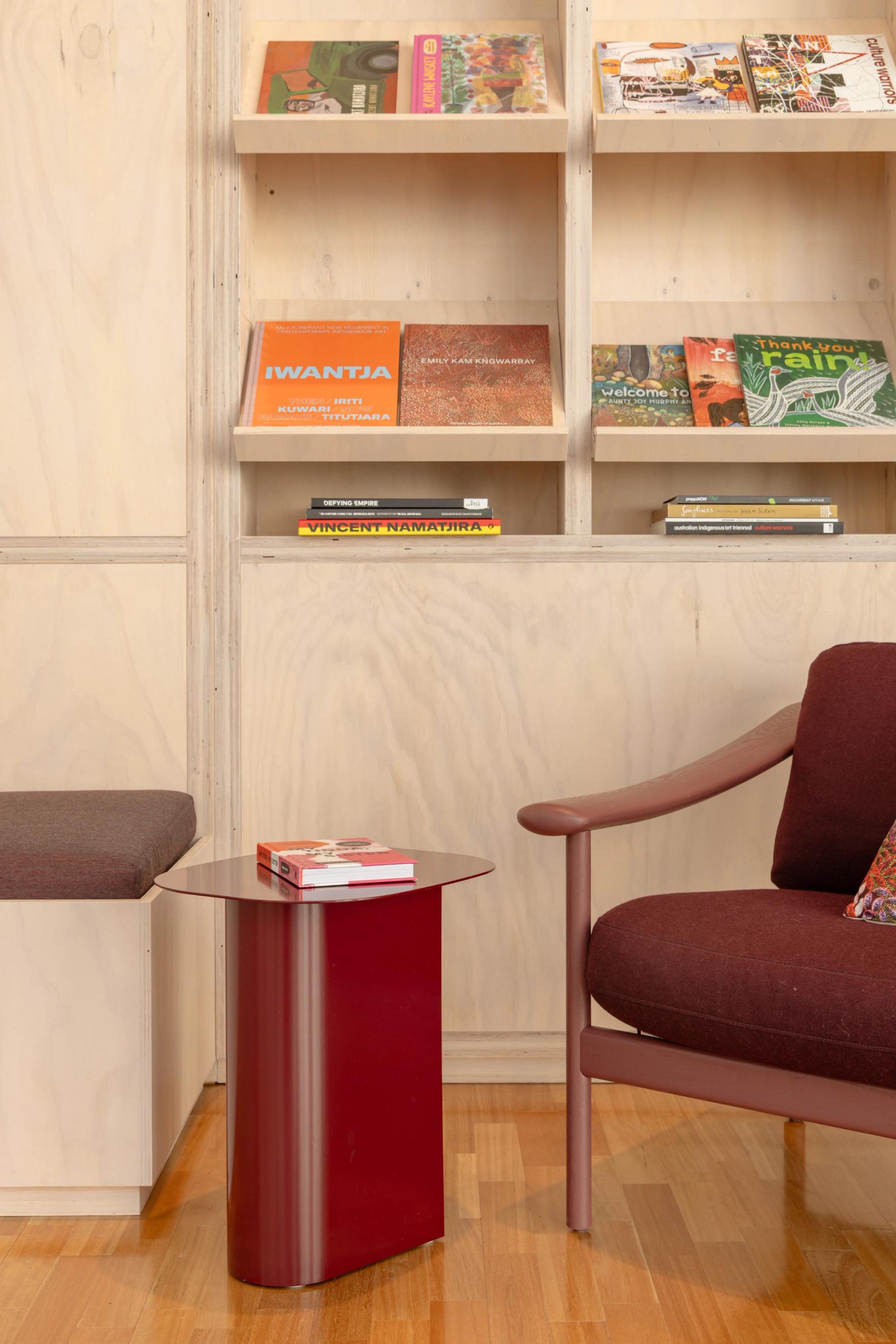 Close up of a room with light wooden shelving with books, red arm chair and red side table.