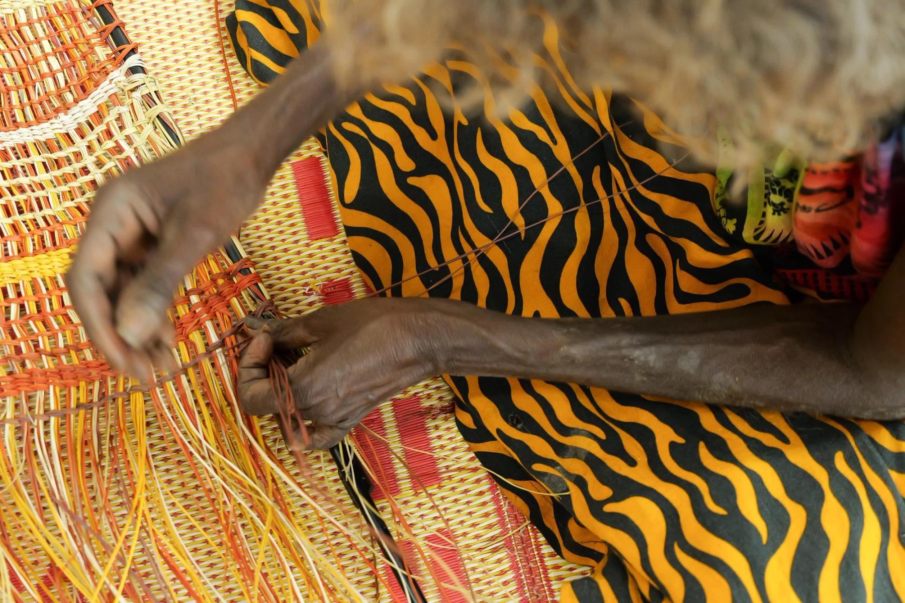 Close up of hands weaving with orange toned fibres.