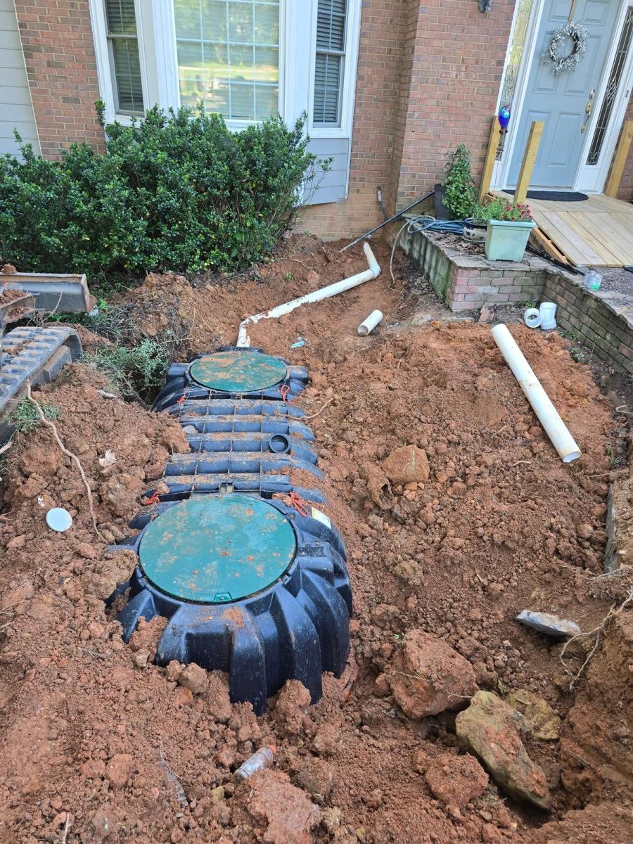 New septic tank set in an open pit beside a brick home — before backfill