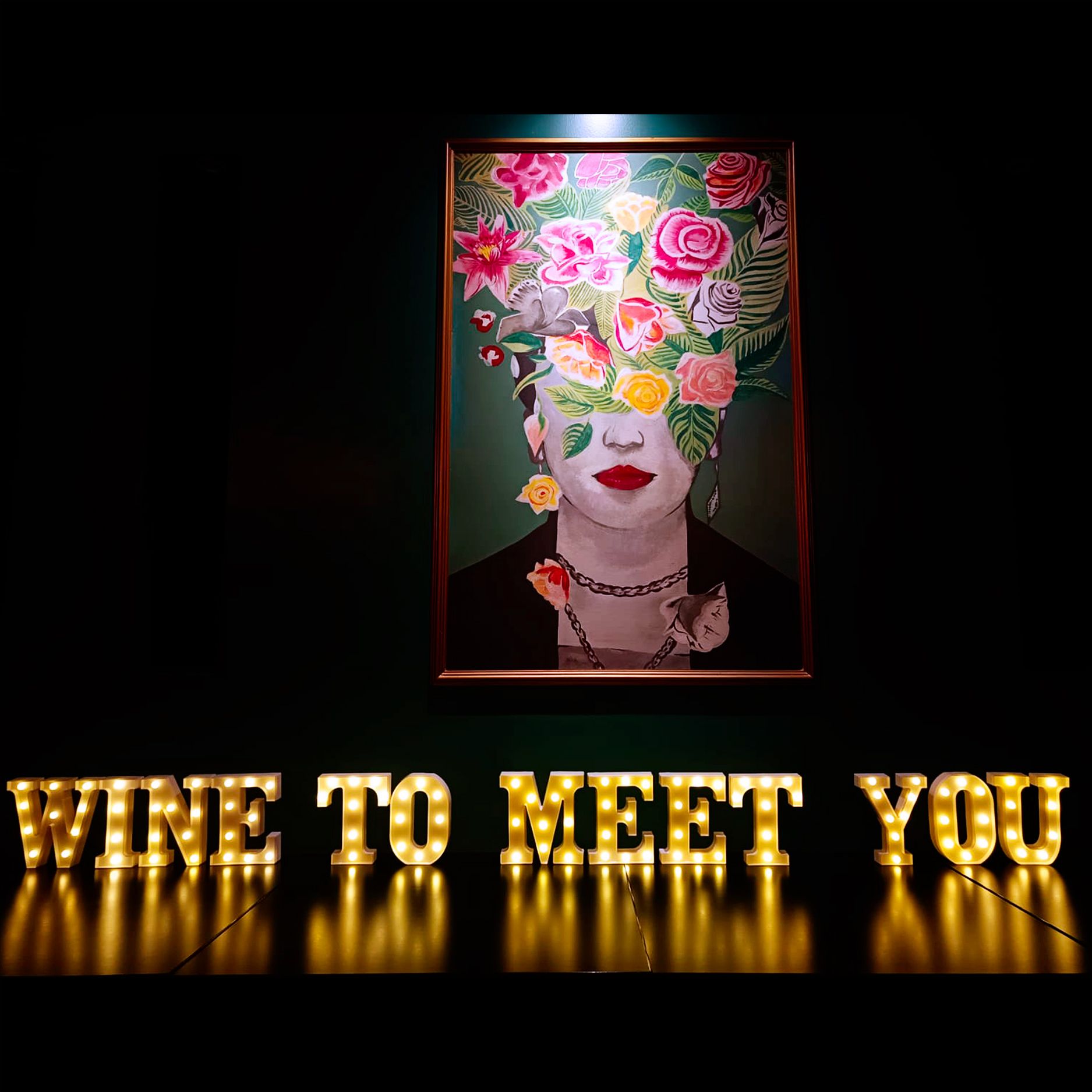 Il quadro della donna con i fiori tra i capelli sopra l'insegna luminosa Wine to meet you