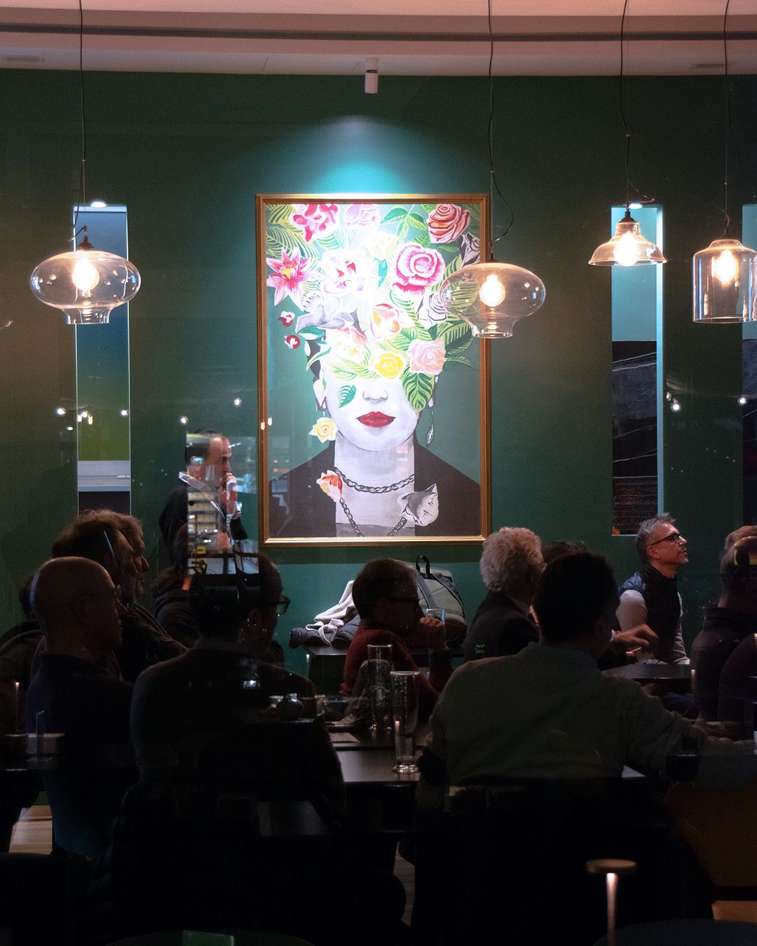 La sala la sera, piena di gente sotto il quadro con i fiori