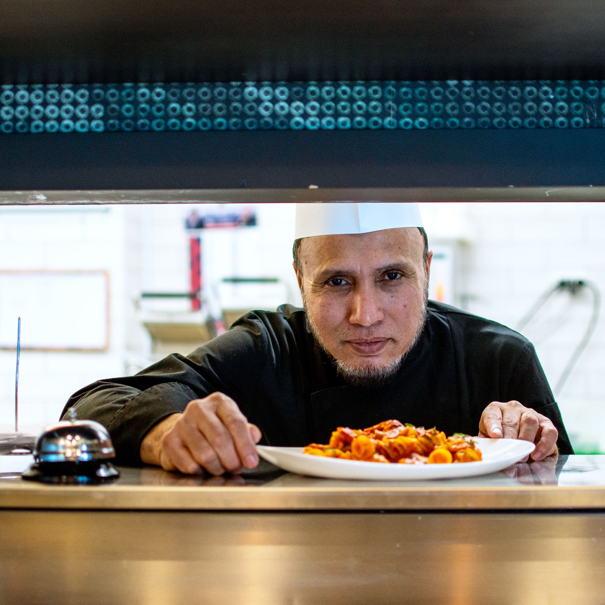 Lo chef porge un piatto di pasta dal pass della cucina