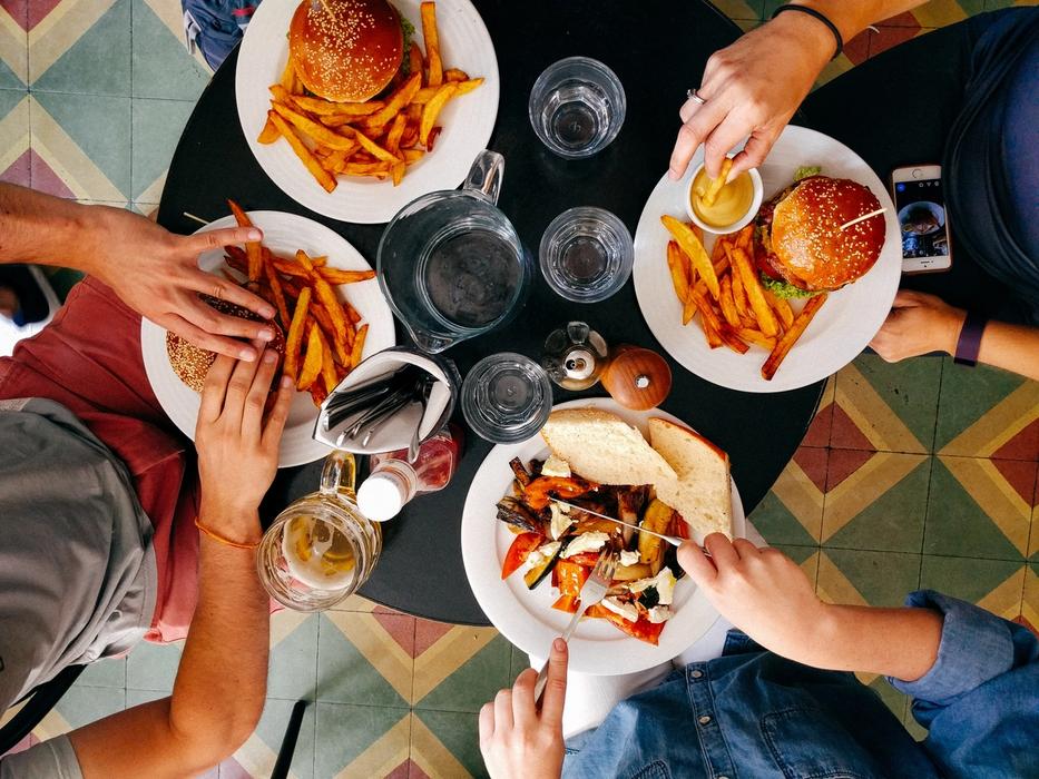 group of four people eating at a small round black table eating burgers and fries, only their hands and food showing.