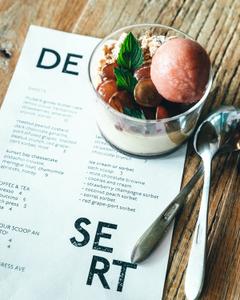 white desert menu on wooden table with a small glass bowl of yogurt and granola