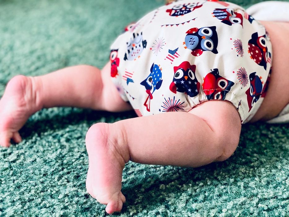 Bottom half of crawling baby wearing an owl-themed cloth diaper