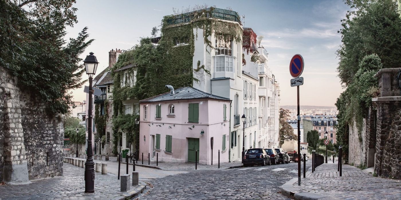 Narrow cobblestone street in Montmartre with historic Parisian buildings and Sacré-Cœur in the background