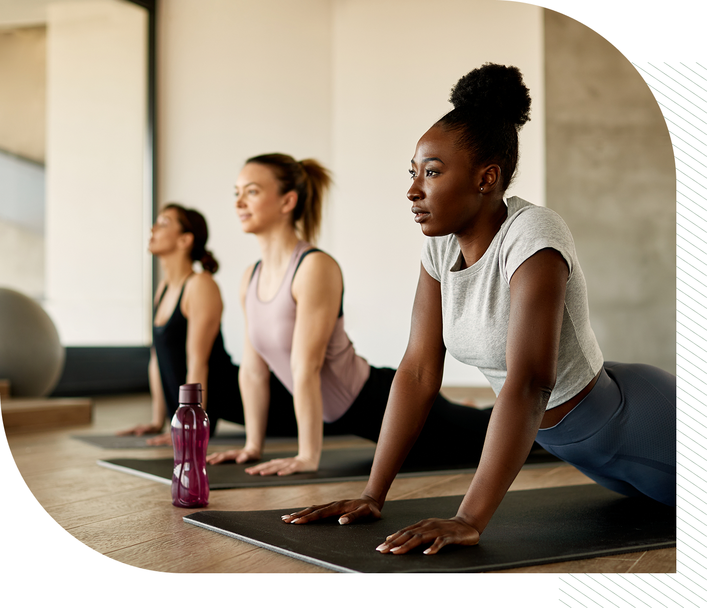 Three women practicing yoga in a bright studio, performing cobra pose on black mats.