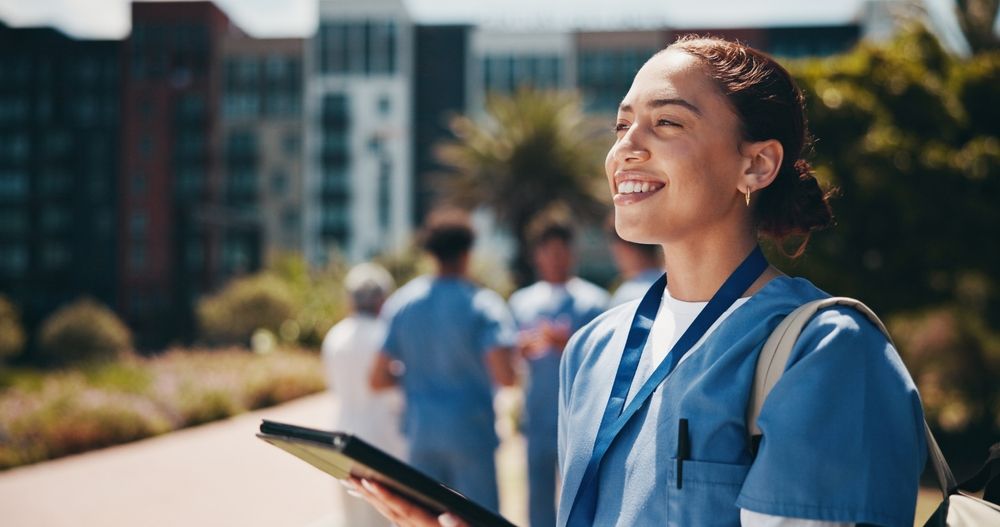Medical student in blue scrubs holding a tablet outdoors, representing study prep with question banks for preclinical students.