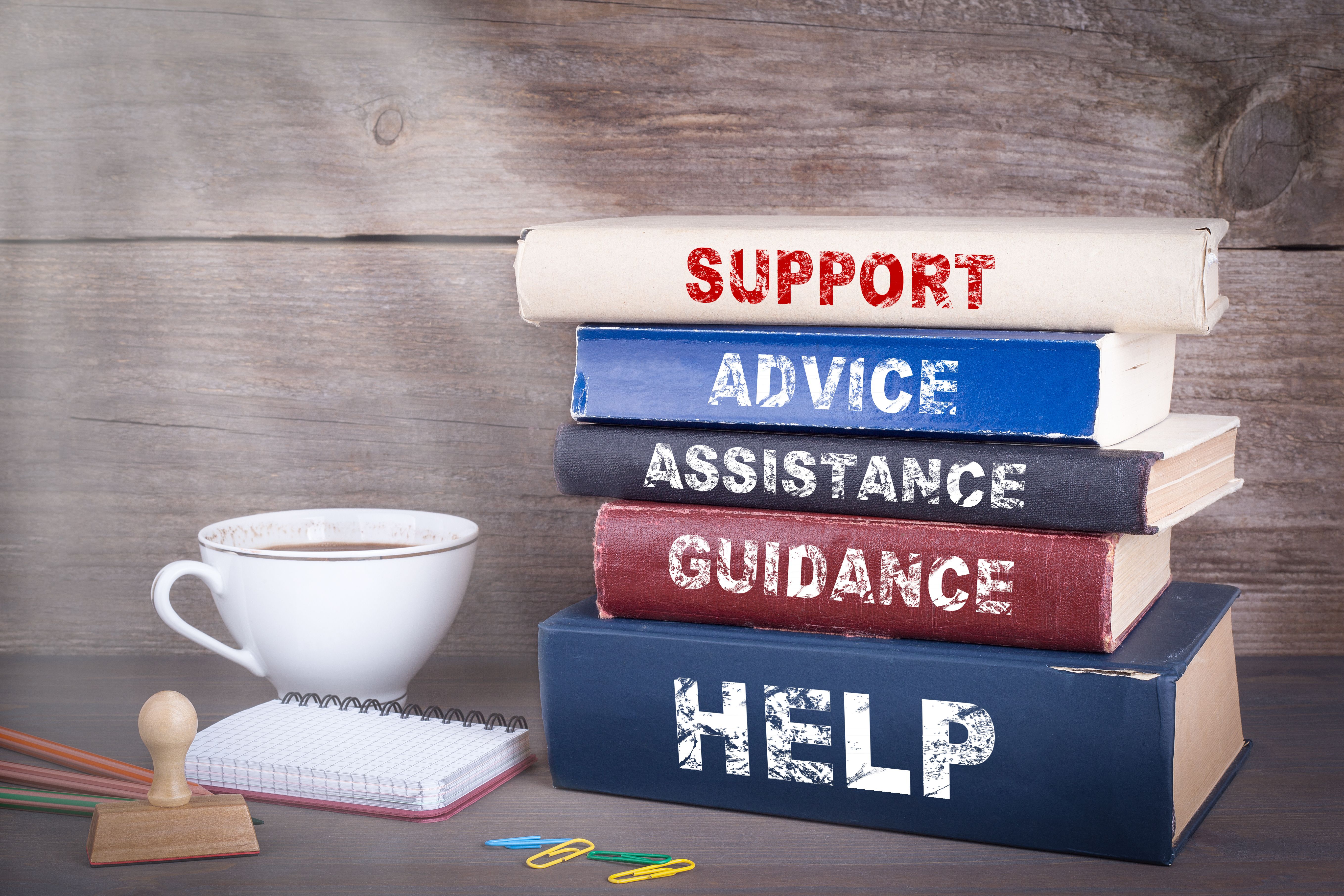 Stack of books titled "Support," "Advice," "Assistance," "Guidance," and "Help" with a coffee cup, notepad, and clips.