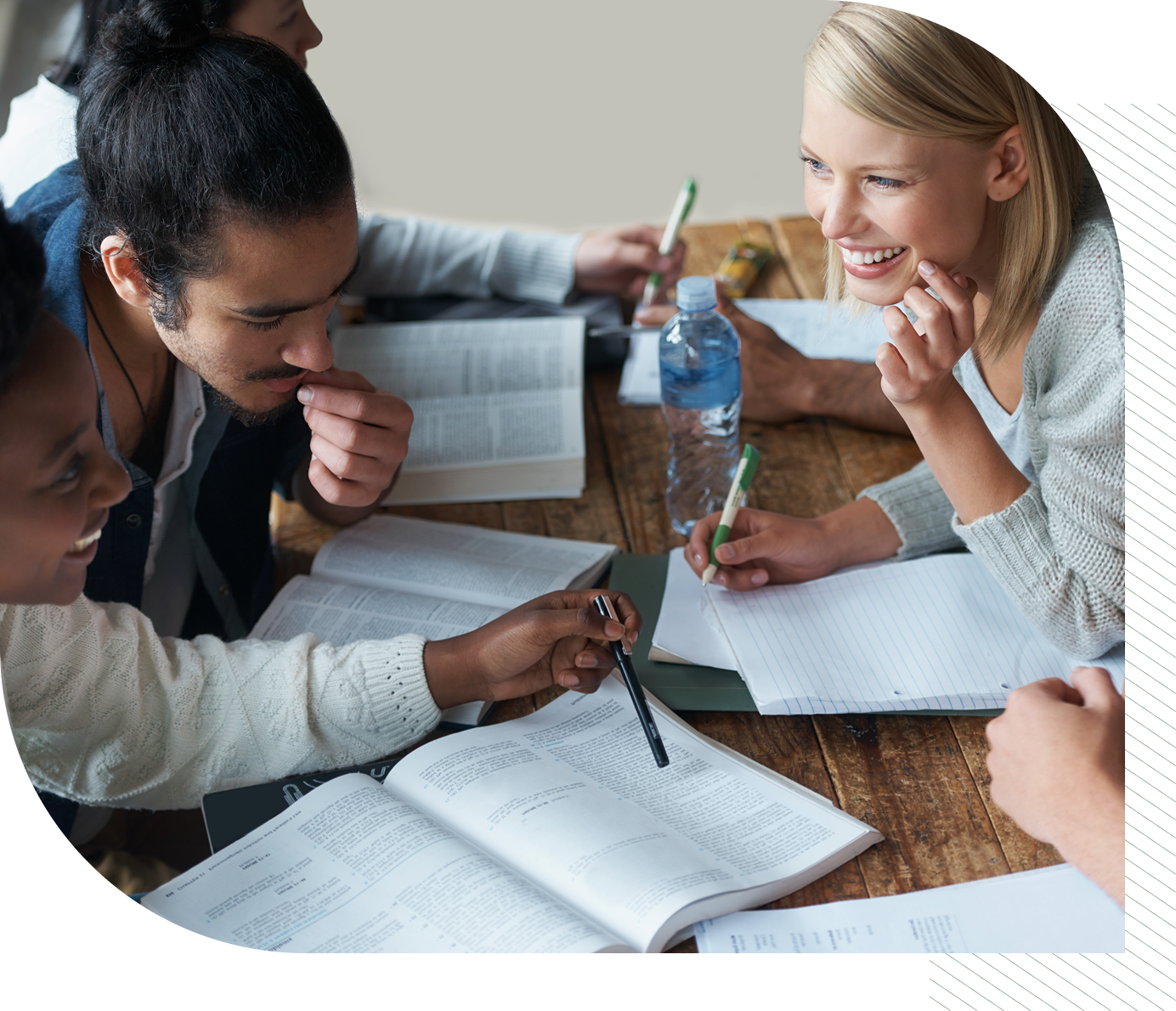A group of diverse students study together with books, pens, and a water bottle on a wooden table.