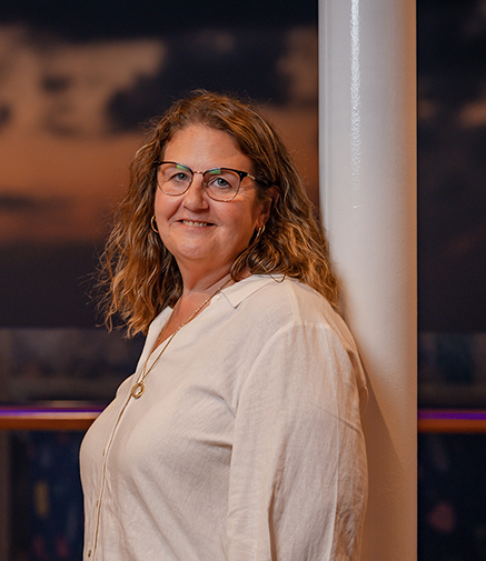 Woman with glasses in a light shirt stands by a white pole, smiling at the camera.