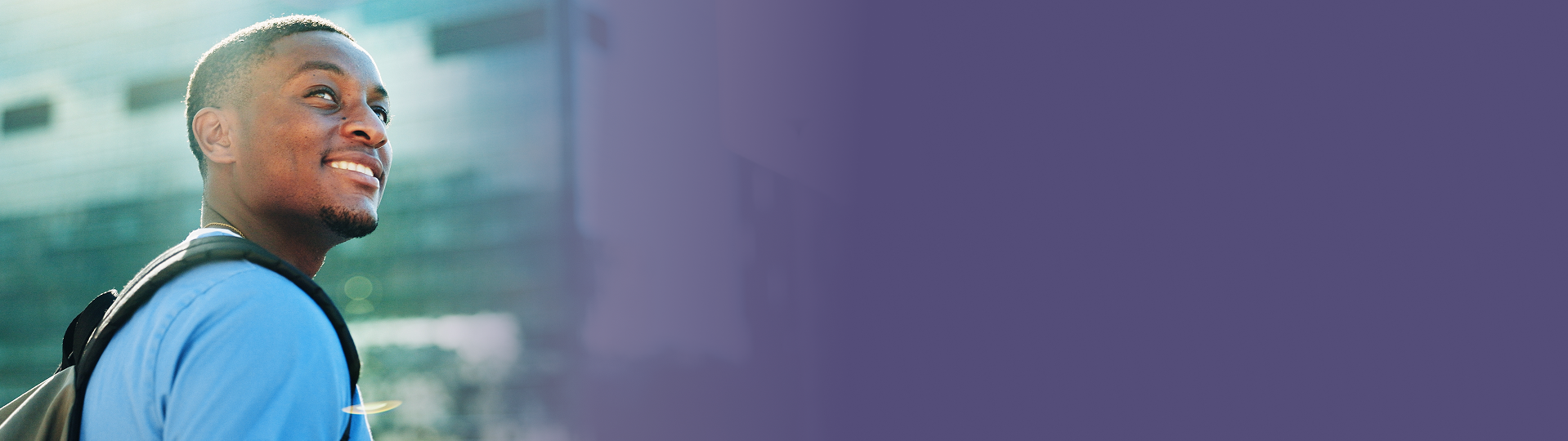 Smiling Black man with backpack looking up outdoors, blurred building background with purple backdrop.