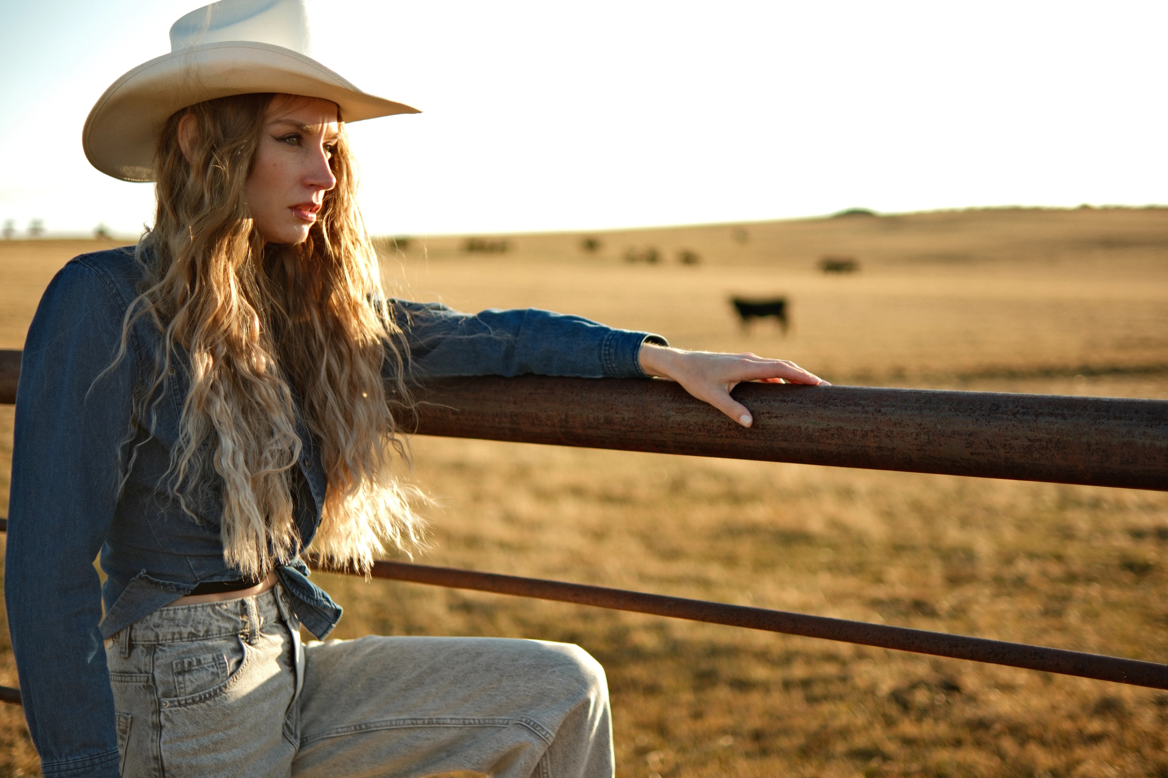 Side profile of woman with cowboy hat touching fence, rural Alberta pasture
