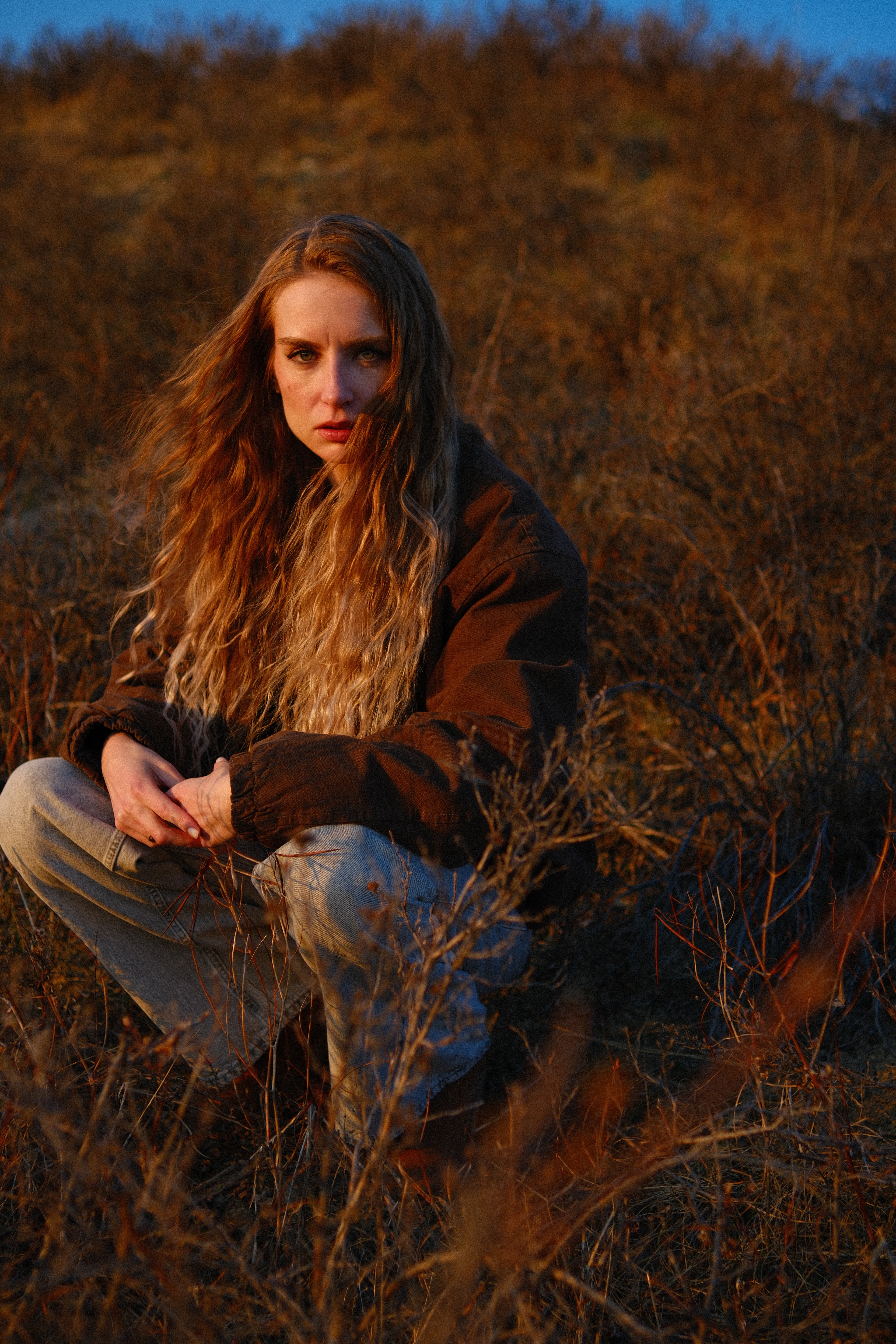 Close-up outdoor portrait of model Mariana sitting in rustic golden fields during sunset, natural light photography.