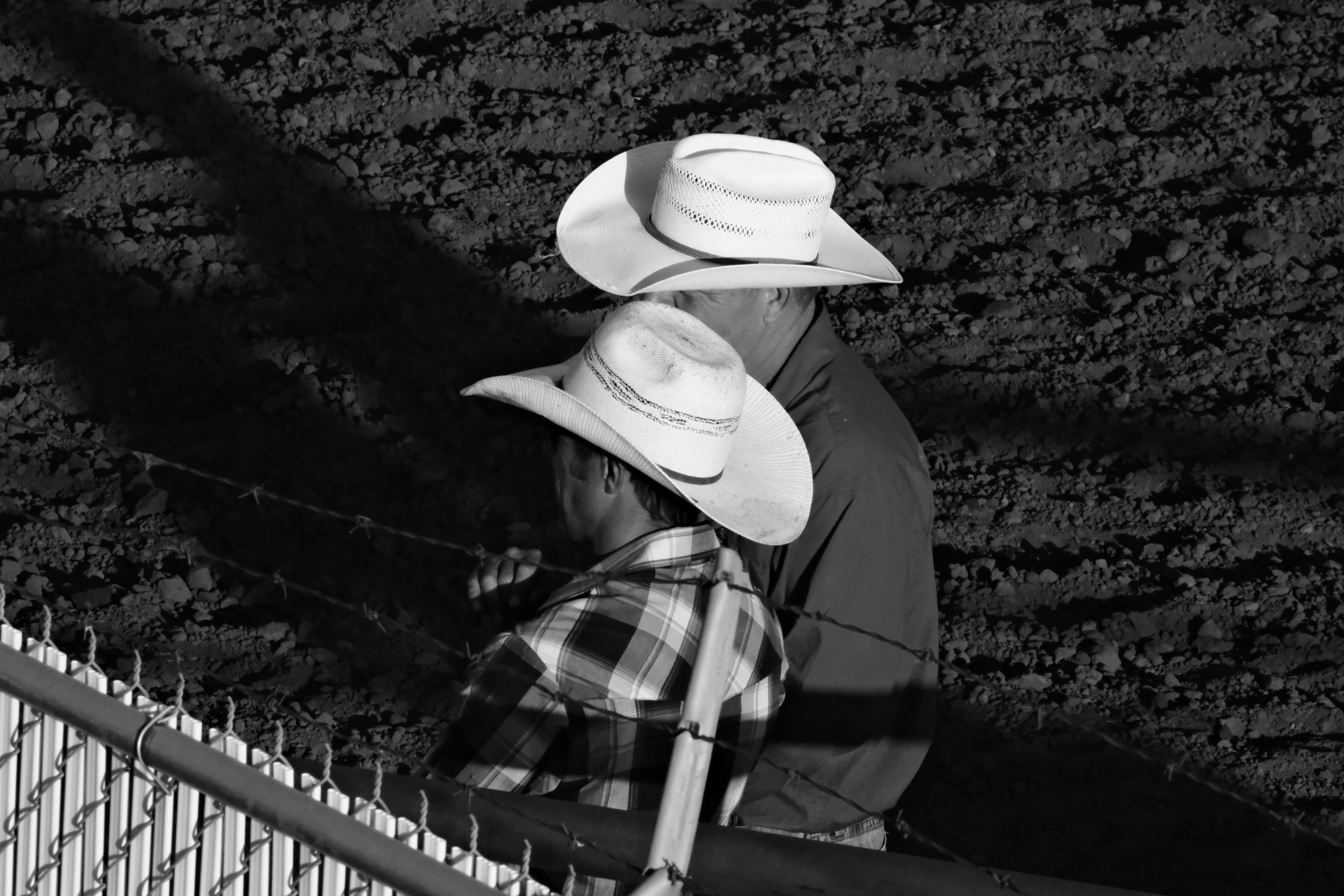 Two people in cowboy hats stand beside the arena fence at Rimbey Rodeo, Alberta.