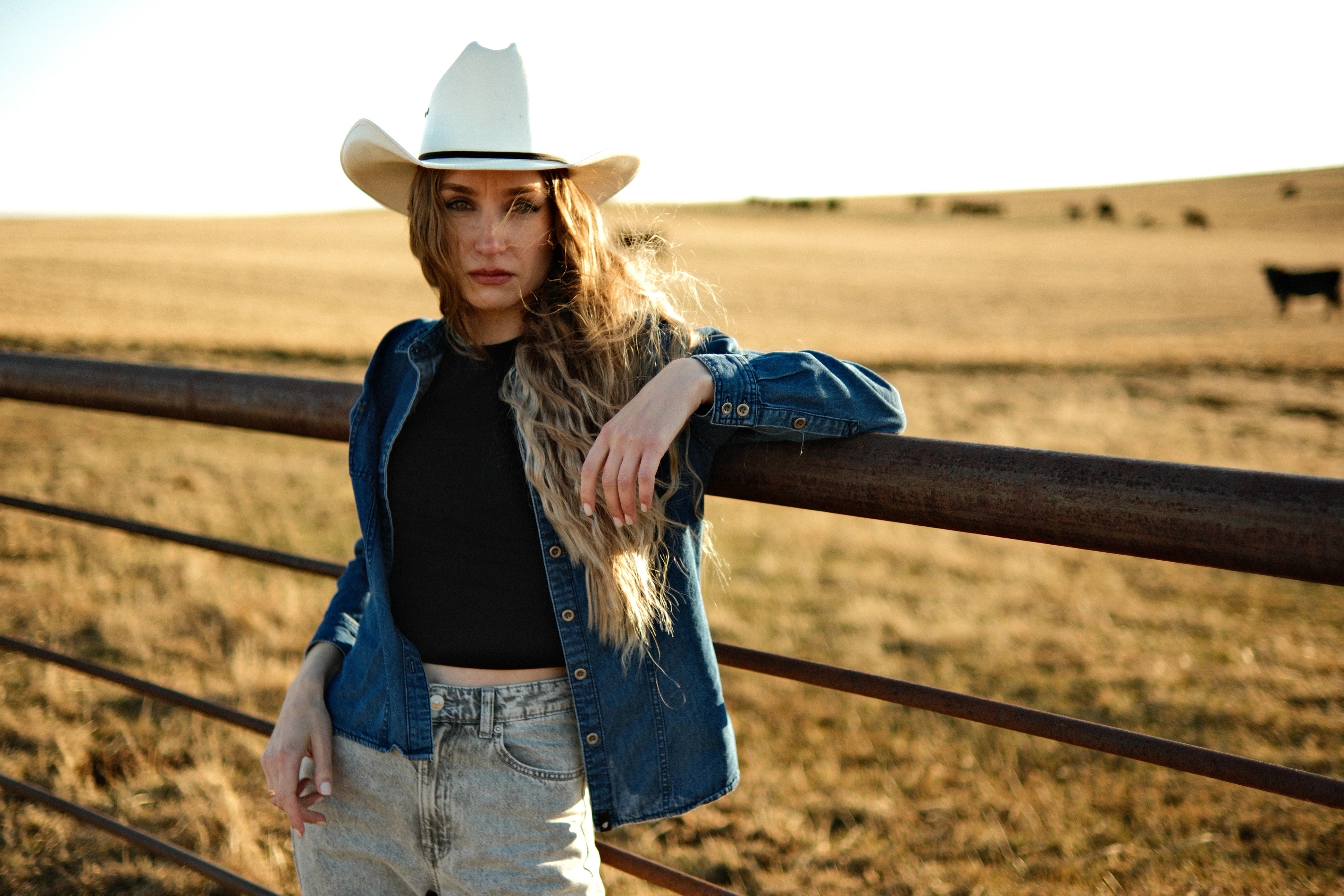 Western-themed portrait of woman leaning on metal fence, Cochrane countryside field