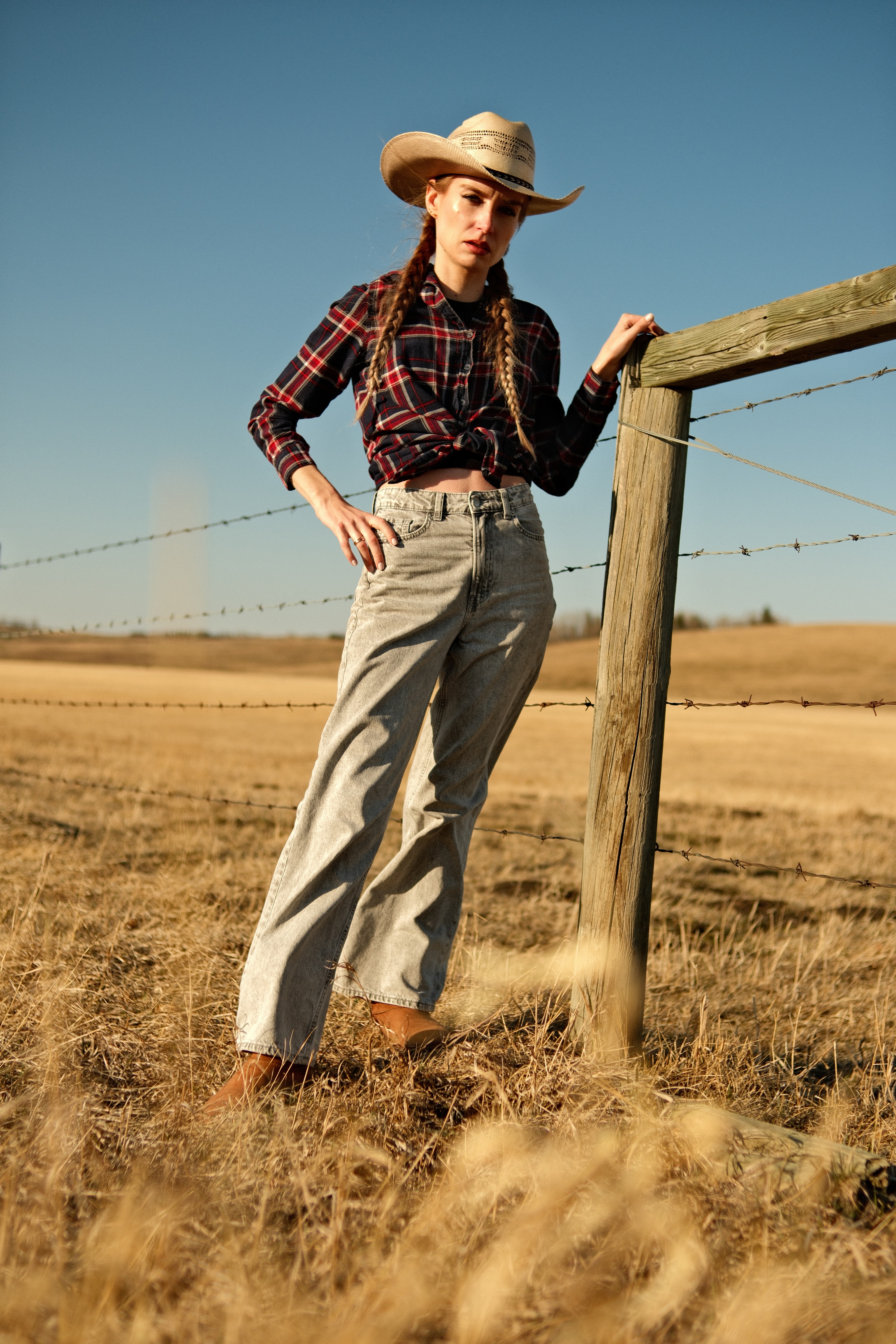 Model wearing a cowboy hat and flannel shirt beside a barbed-wire fence in Cochrane at golden hour.