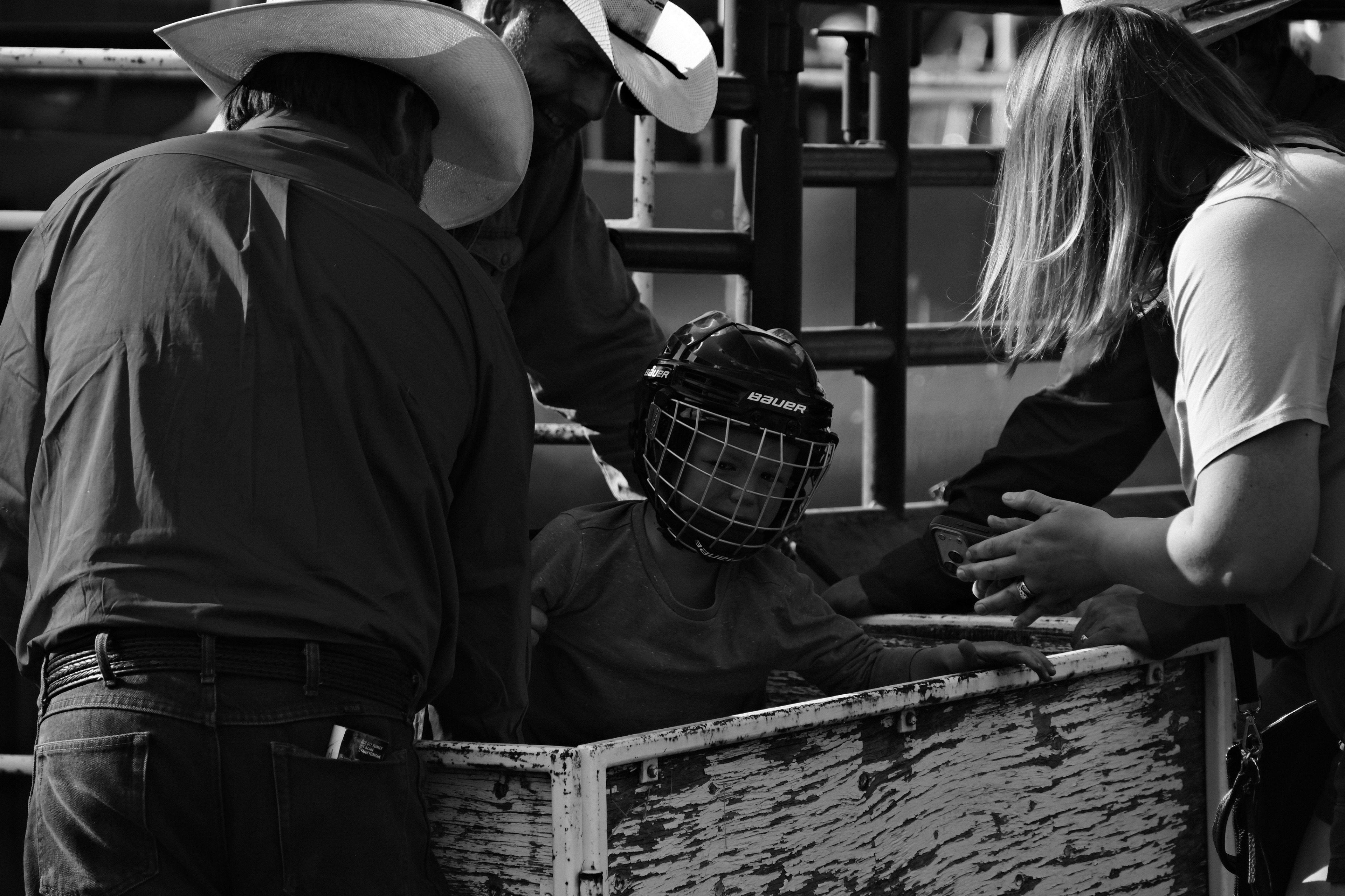 A young rider wearing a protective helmet is helped by adults beside the chute before a rodeo event in Rimbey, Alberta.