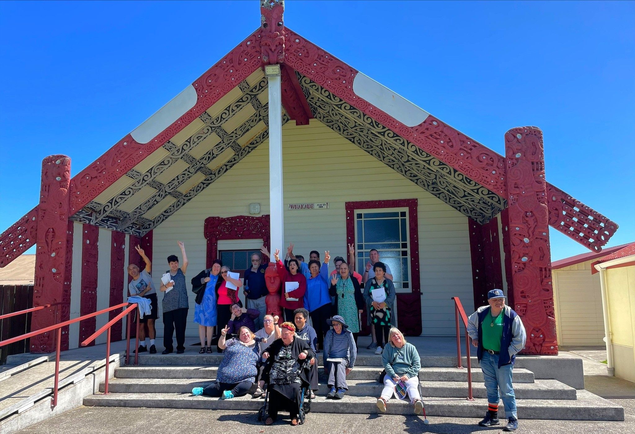 Members outside of a Marae smiling on a sunny day.