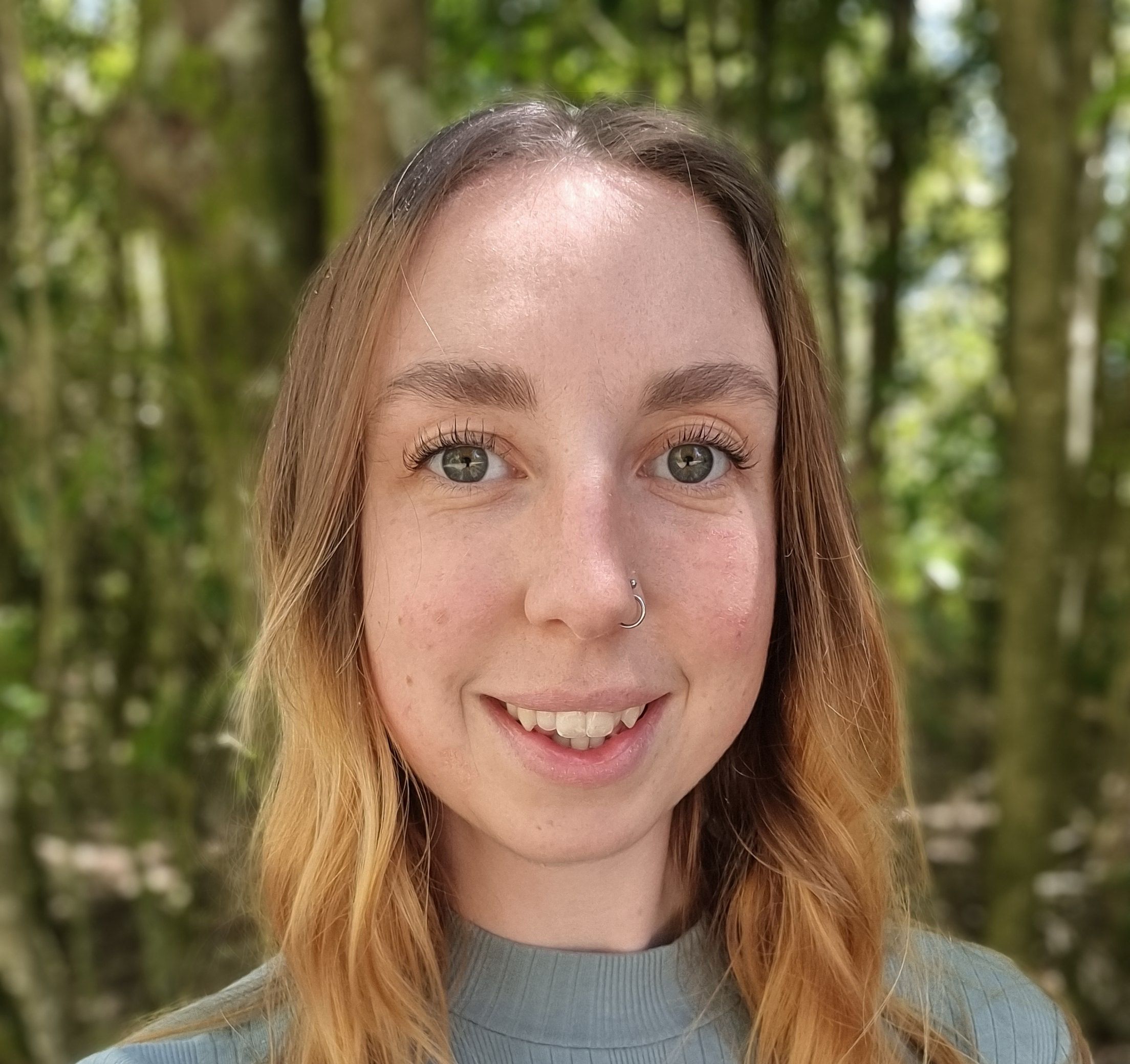 Image of Ellie with a blue top on smiling at camera.