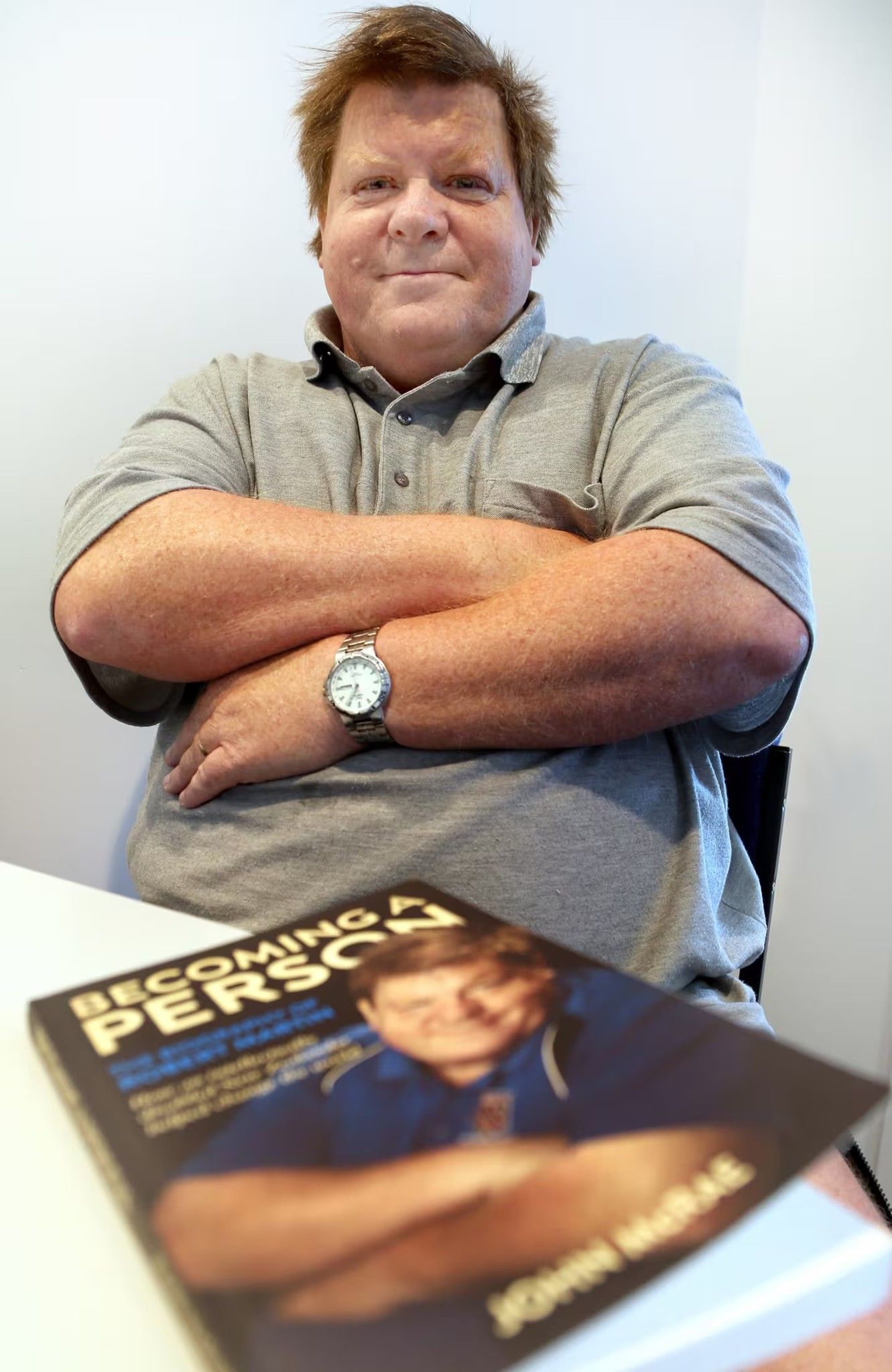 Sir Robert Martin smiling at the camera with his arms corssed while his book is in front of him.