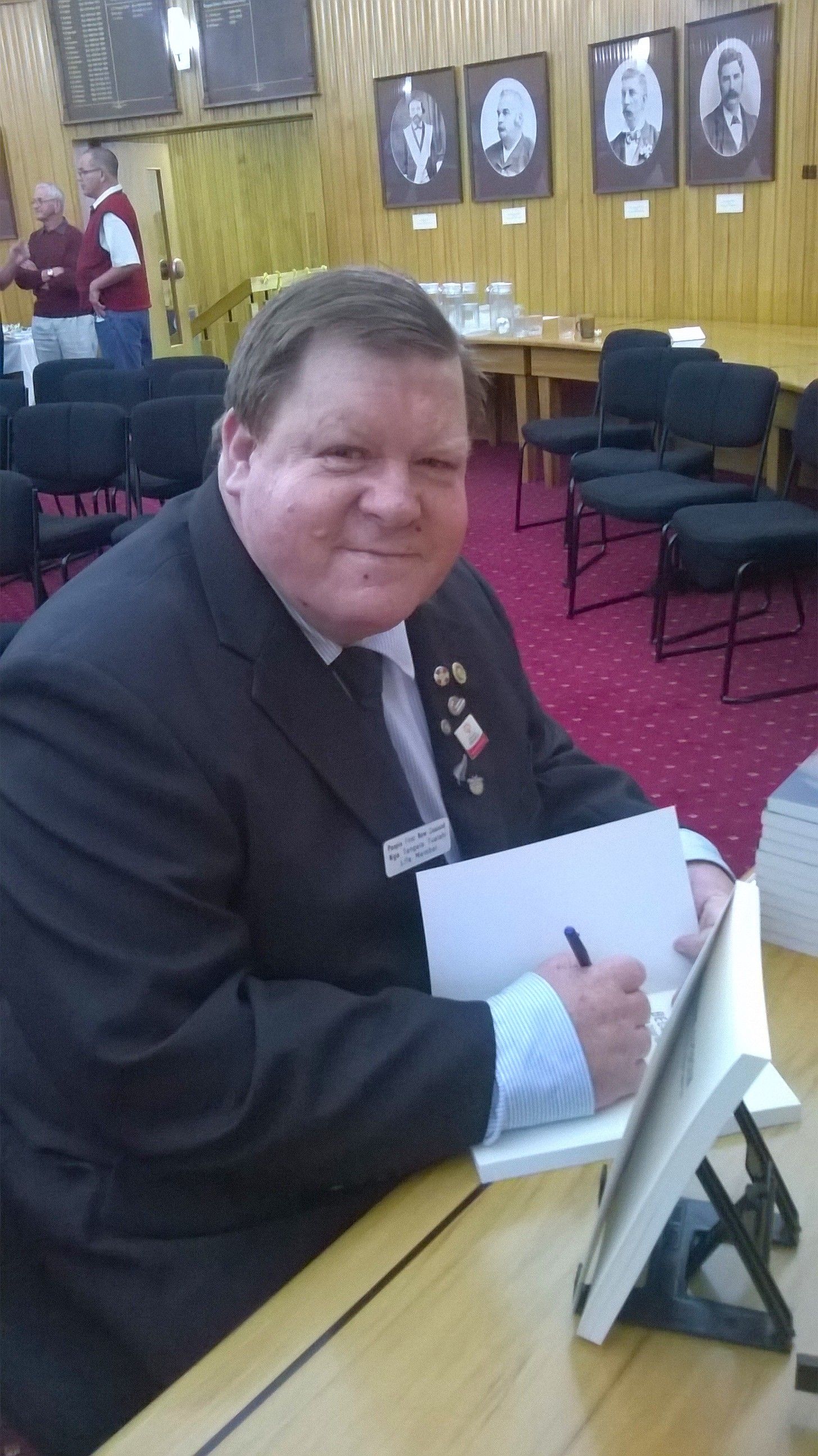 Sir Robert smiling at the camera while signing a book.