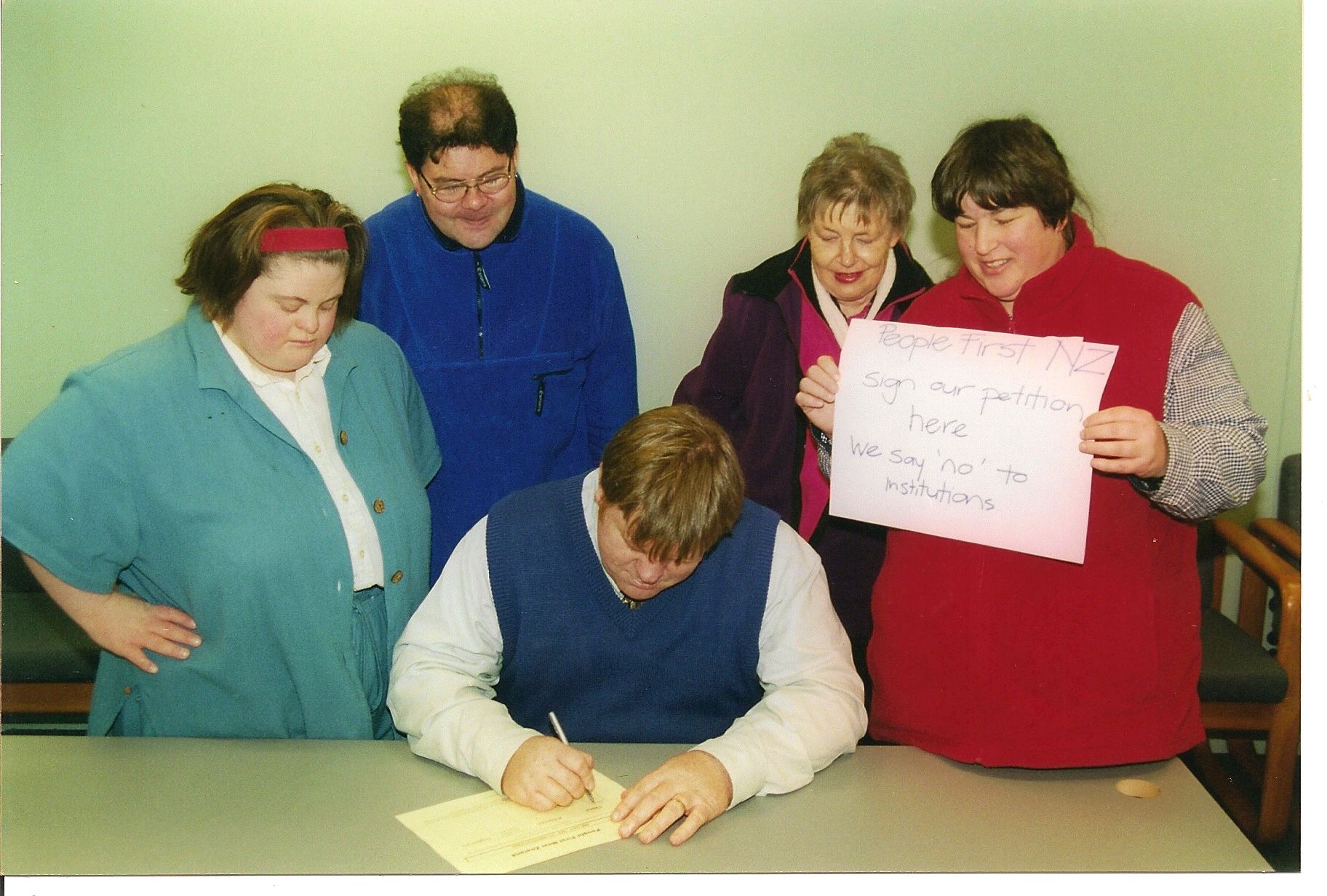 Robert Martin signing a petition surrounded by People First members supporting him.