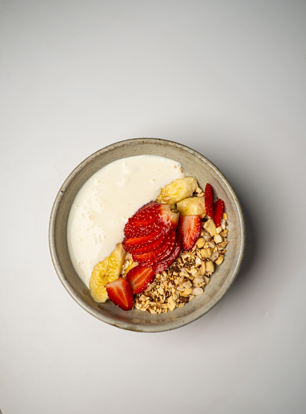 A ceramic bowl of creamy yogurt topped with fresh strawberries, banana chunks, and crunchy granola
