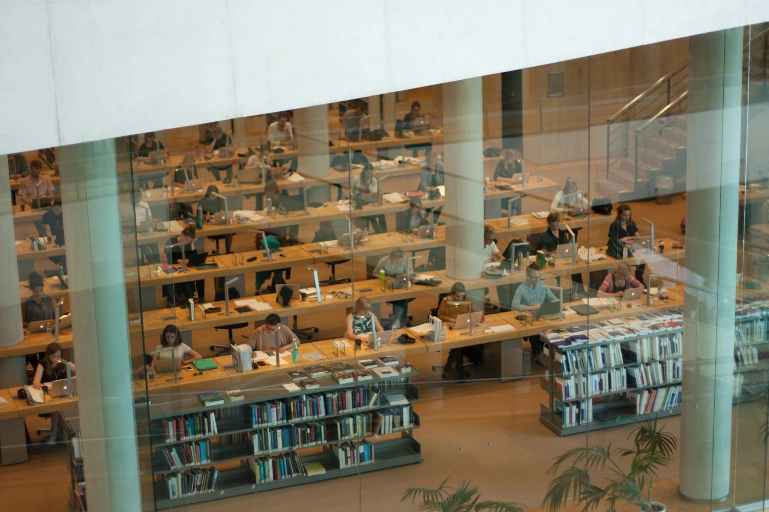 Modern library with many people studying at desks and visible bookshelves.