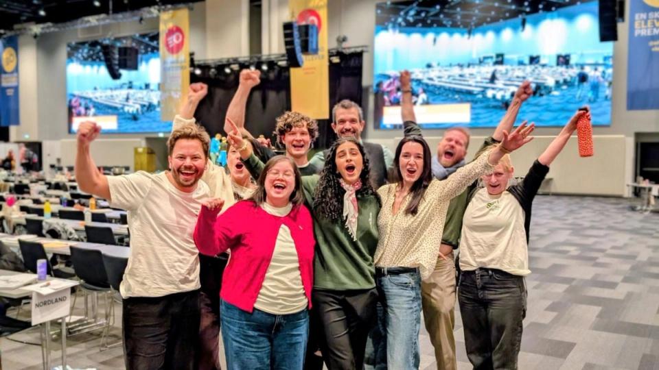 A diverse group of ten people celebrating with raised arms in a large conference hall.