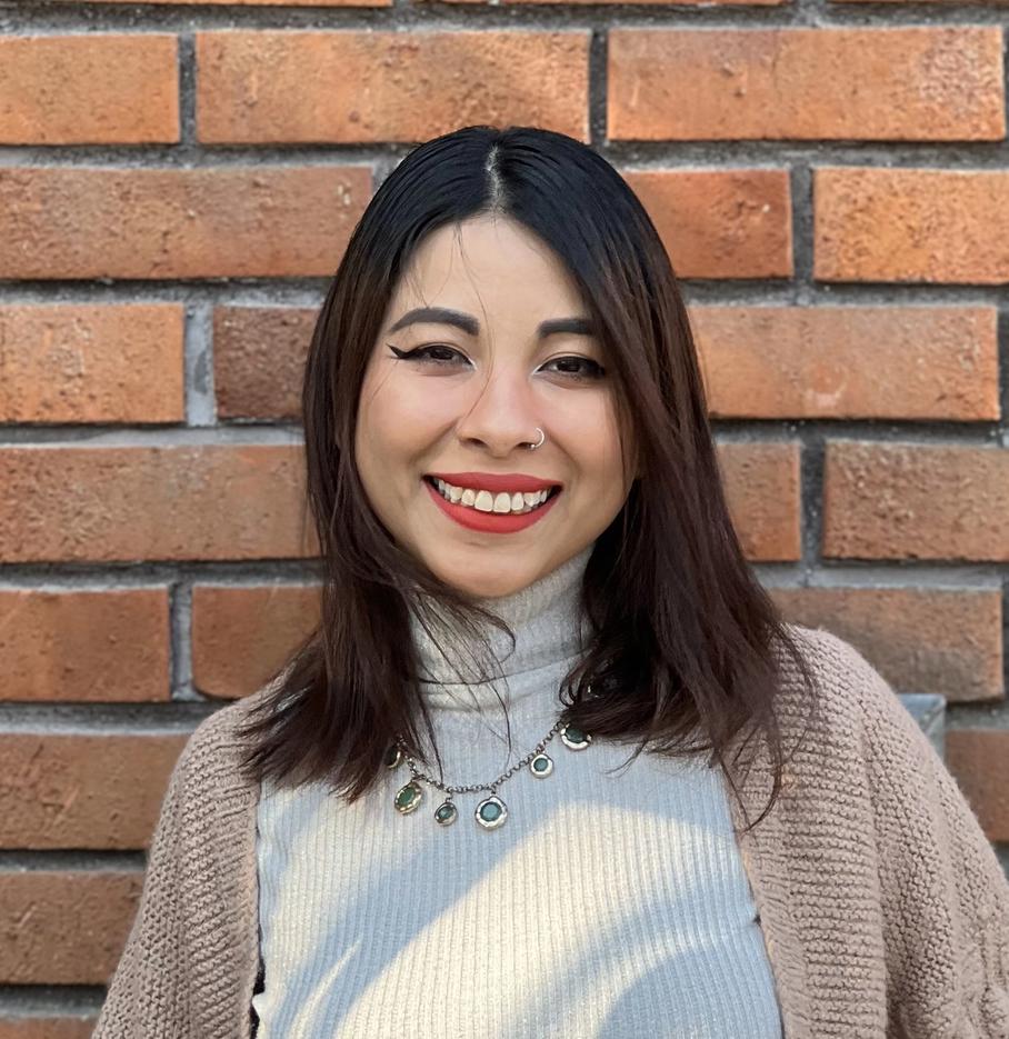 a woman wearing a sweater and jeans is standing in front of a brick wall .