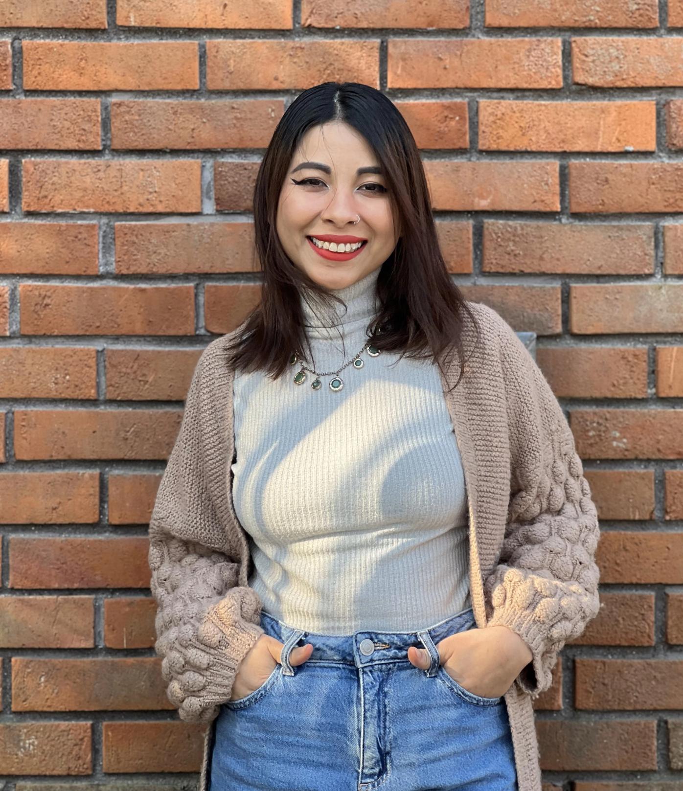 a woman wearing a sweater and jeans is standing in front of a brick wall .