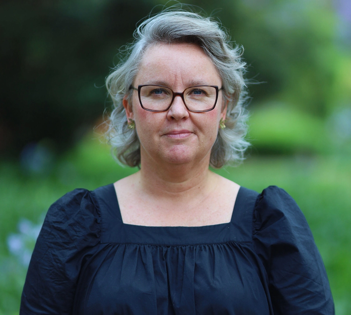 a woman wearing glasses and a black dress smiles for the camera