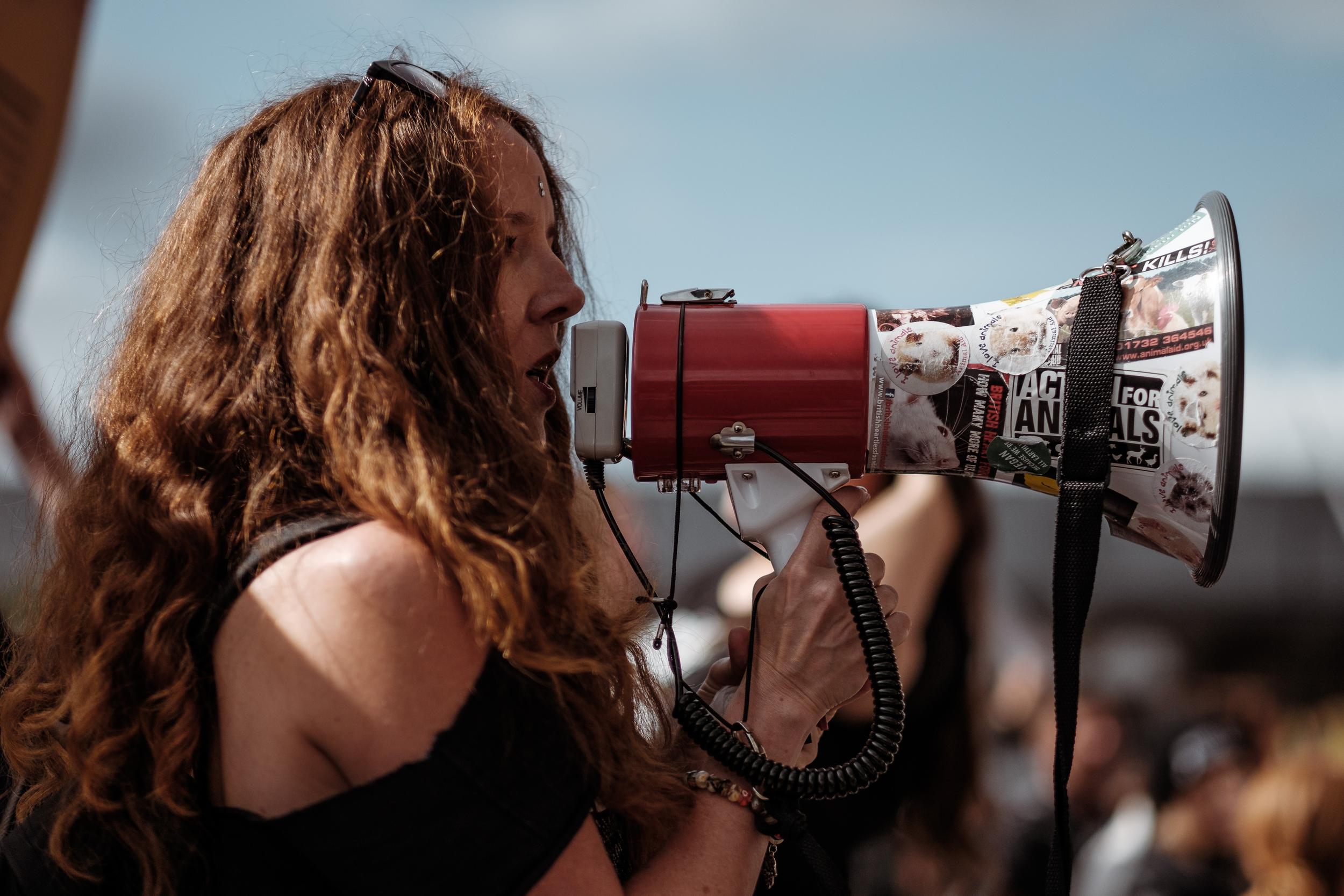En kvinne snakker i en megafon foran en stor forsamling. 