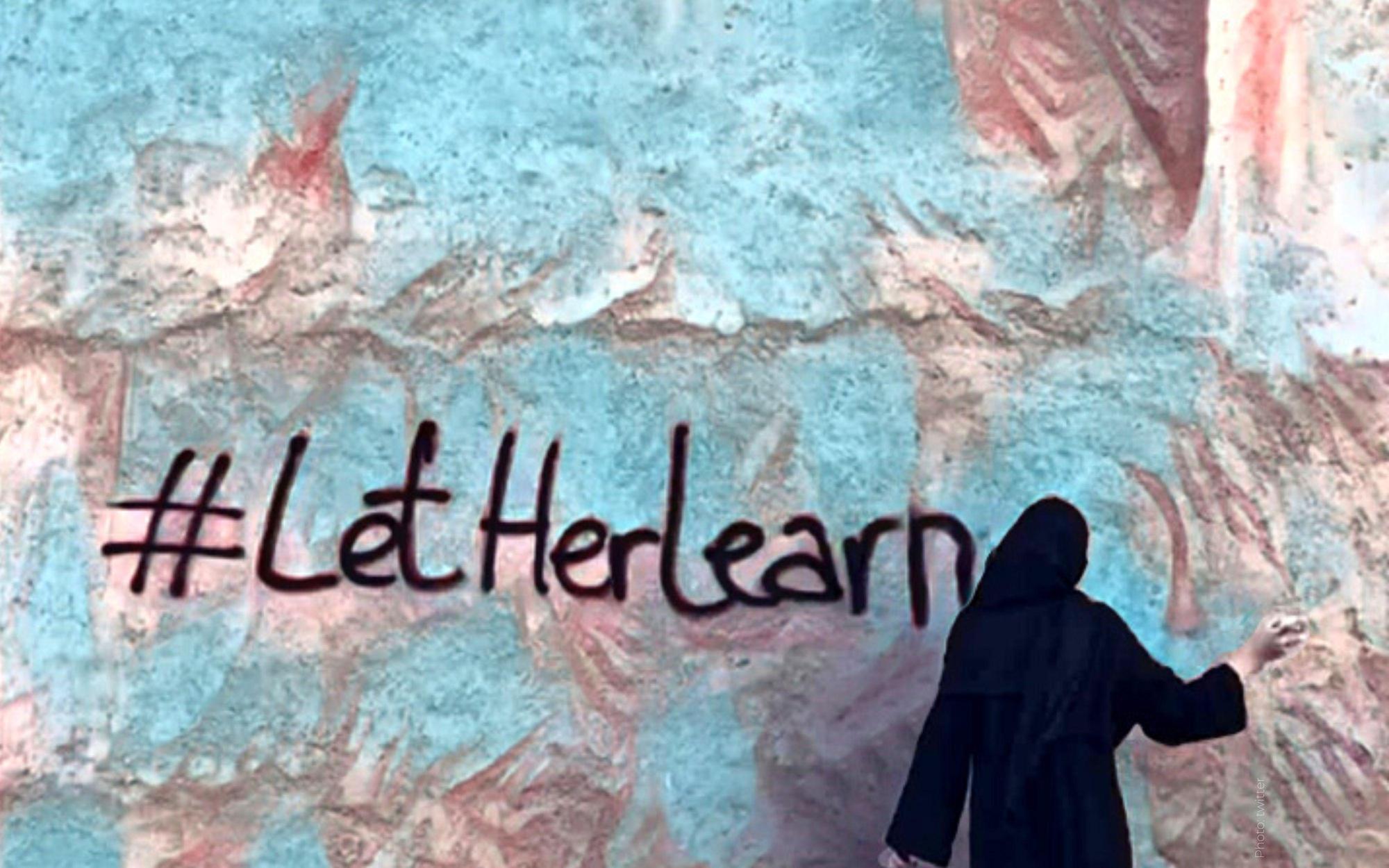 A woman is standing in front of a wall with the words `` let her learn '' written on it.