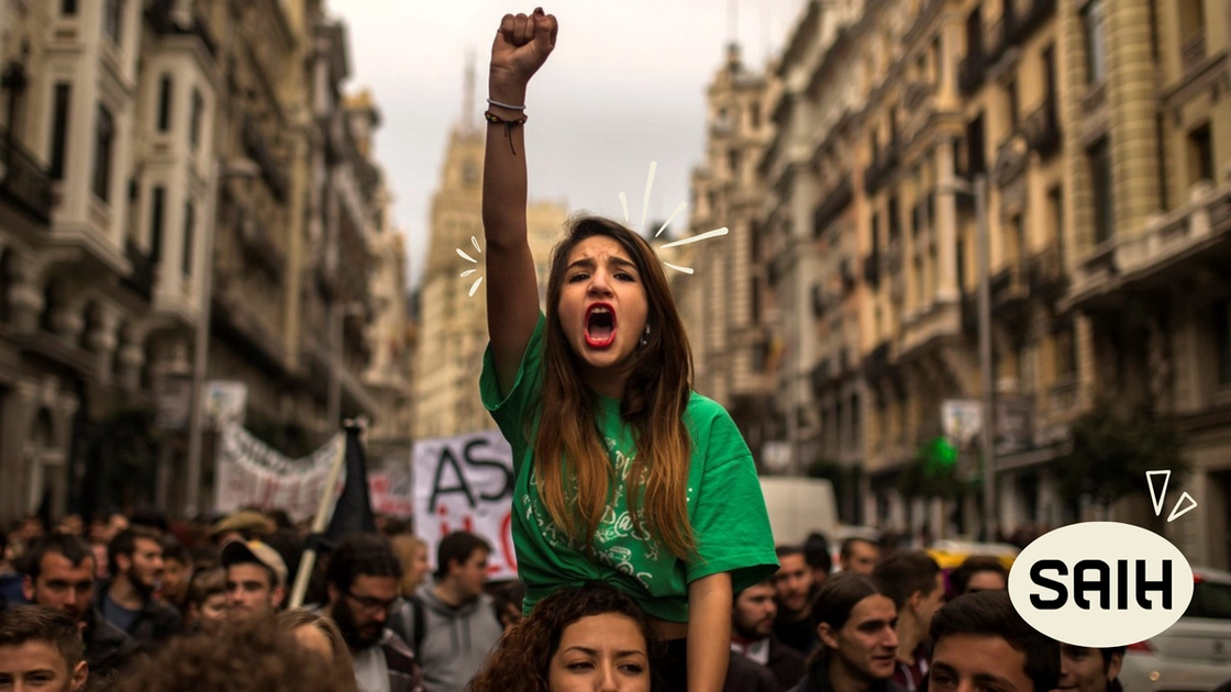 a woman in a green shirt is shouting in front of a crowd with a sign that says saih