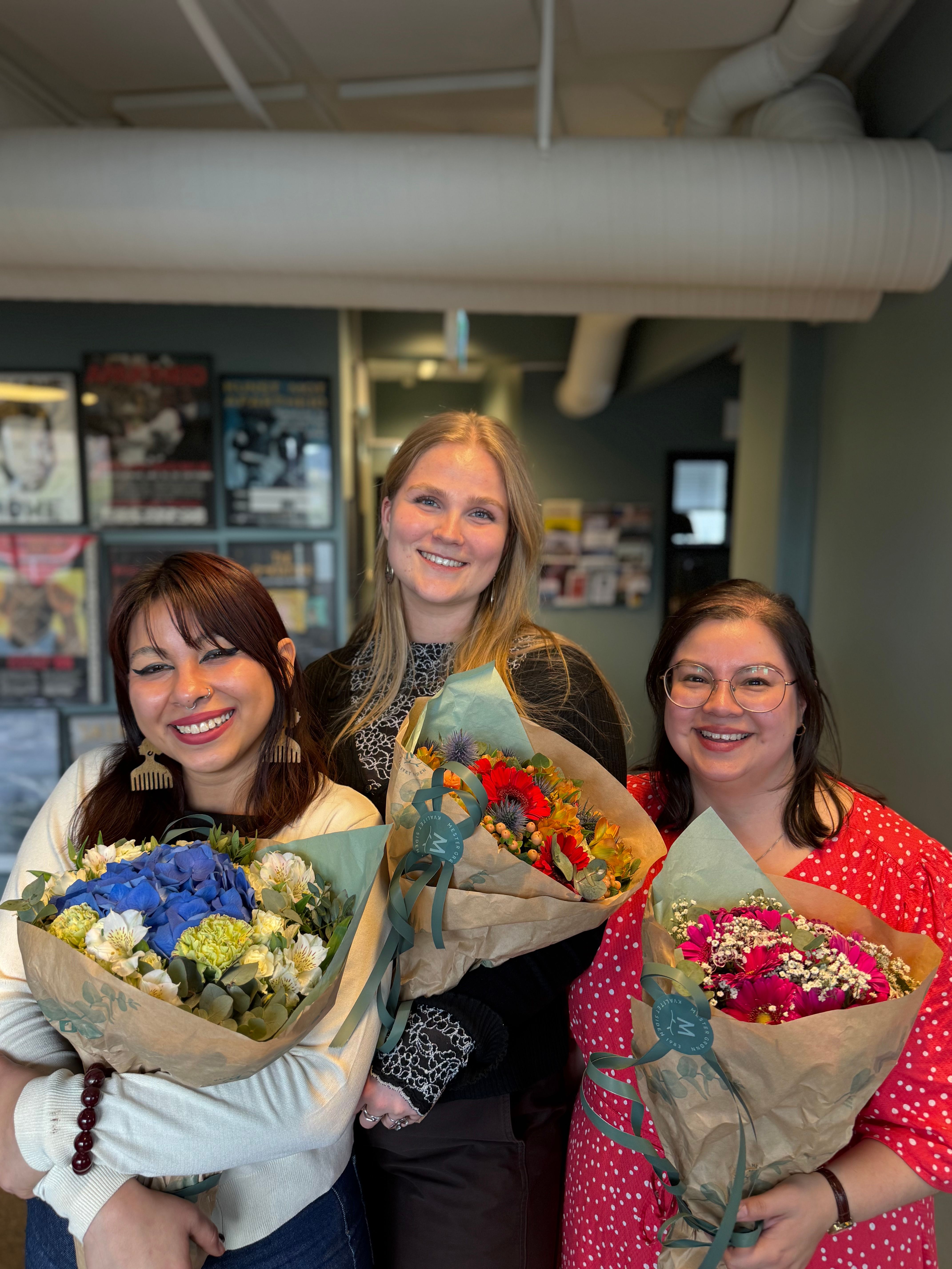 Three smiling women holding colorful flower bouquets.