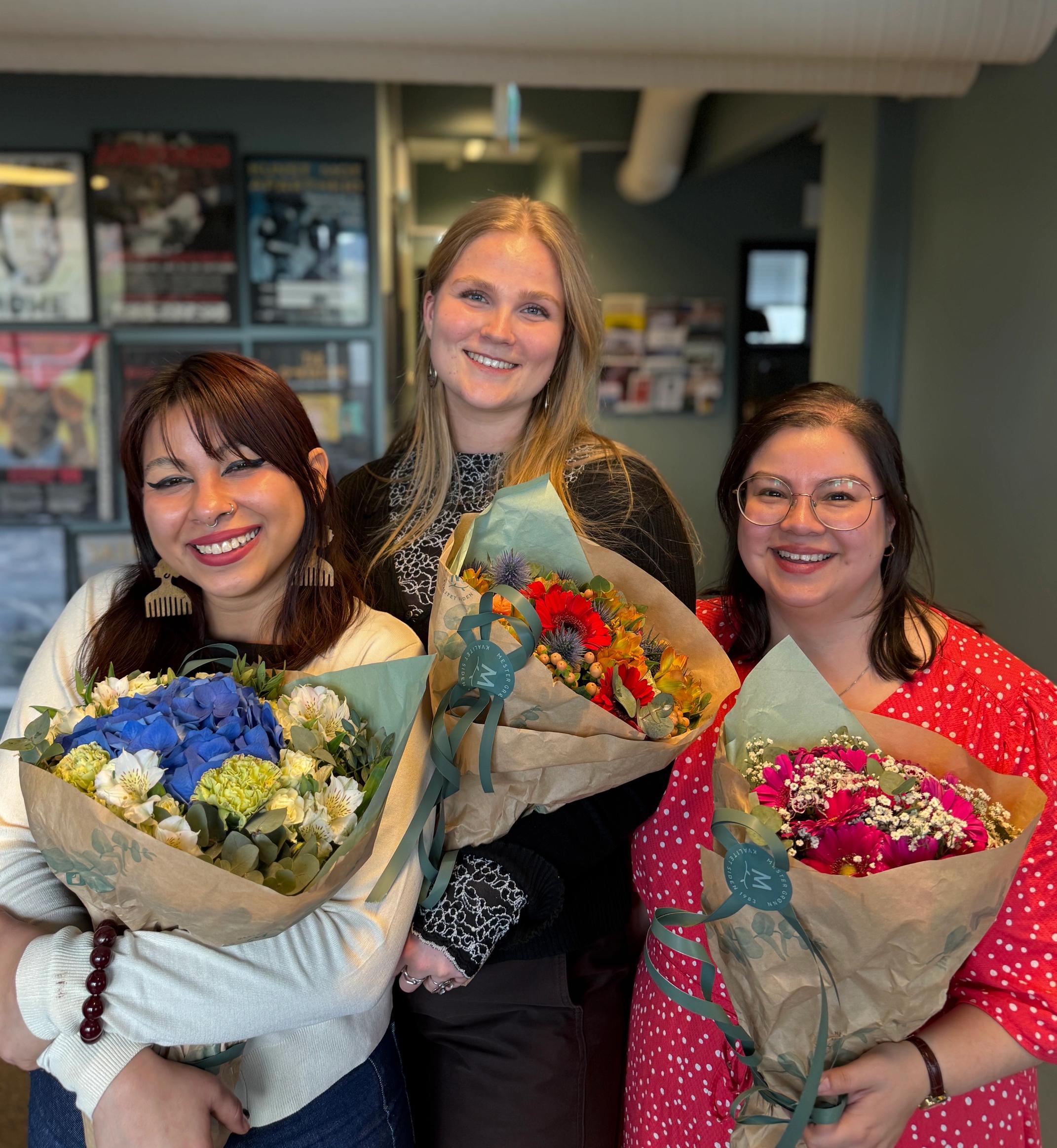 Three smiling women holding colorful flower bouquets.
