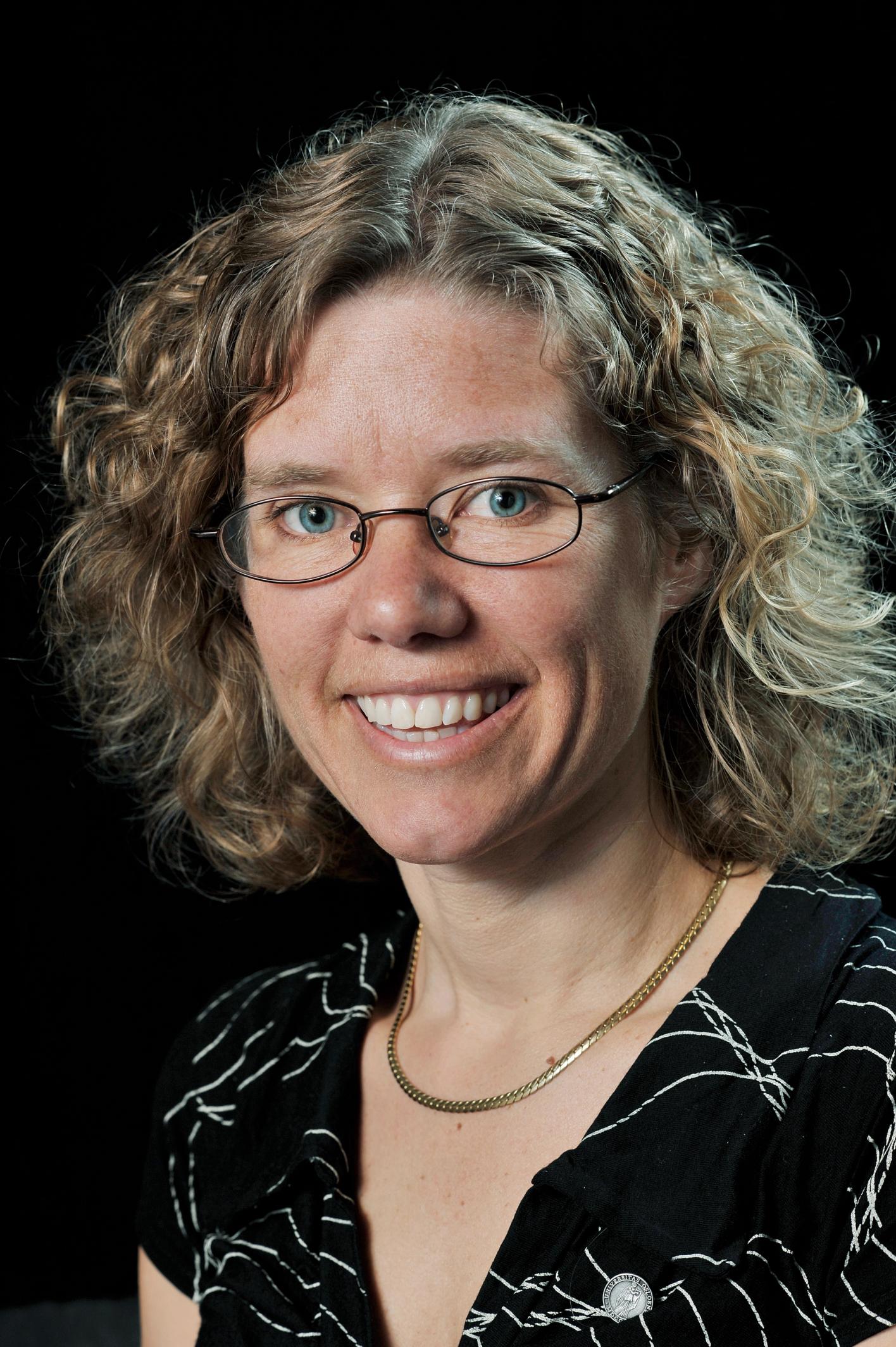 a woman wearing glasses and a necklace smiles for the camera