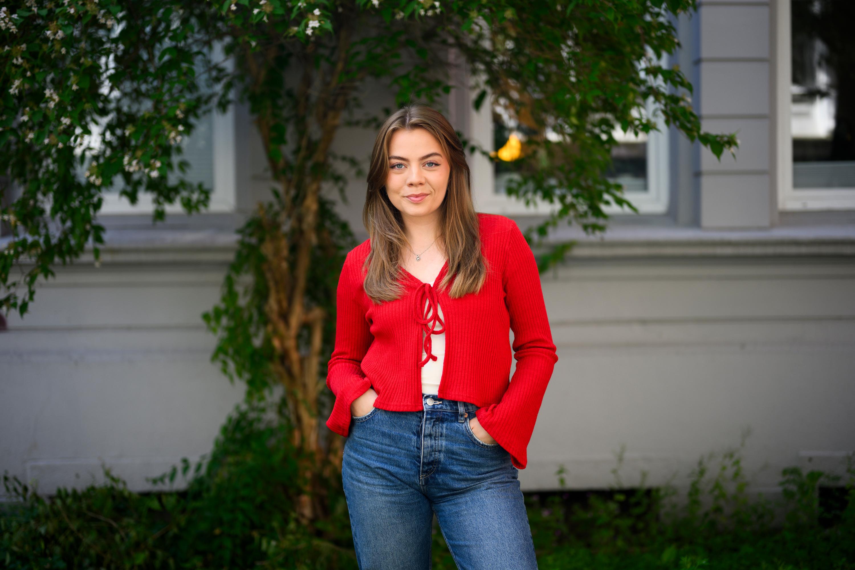 a young woman in a red cardigan and jeans is standing in front of a building .