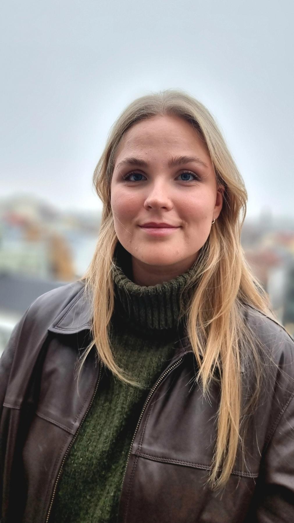 a woman wearing a brown leather jacket and a green sweater