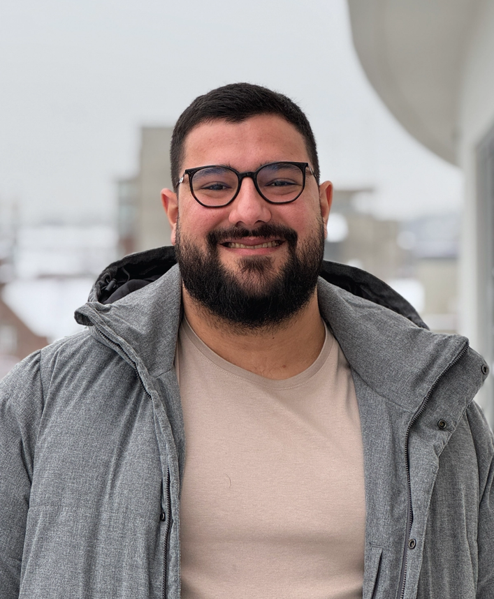 a man with a beard wearing glasses and a grey jacket