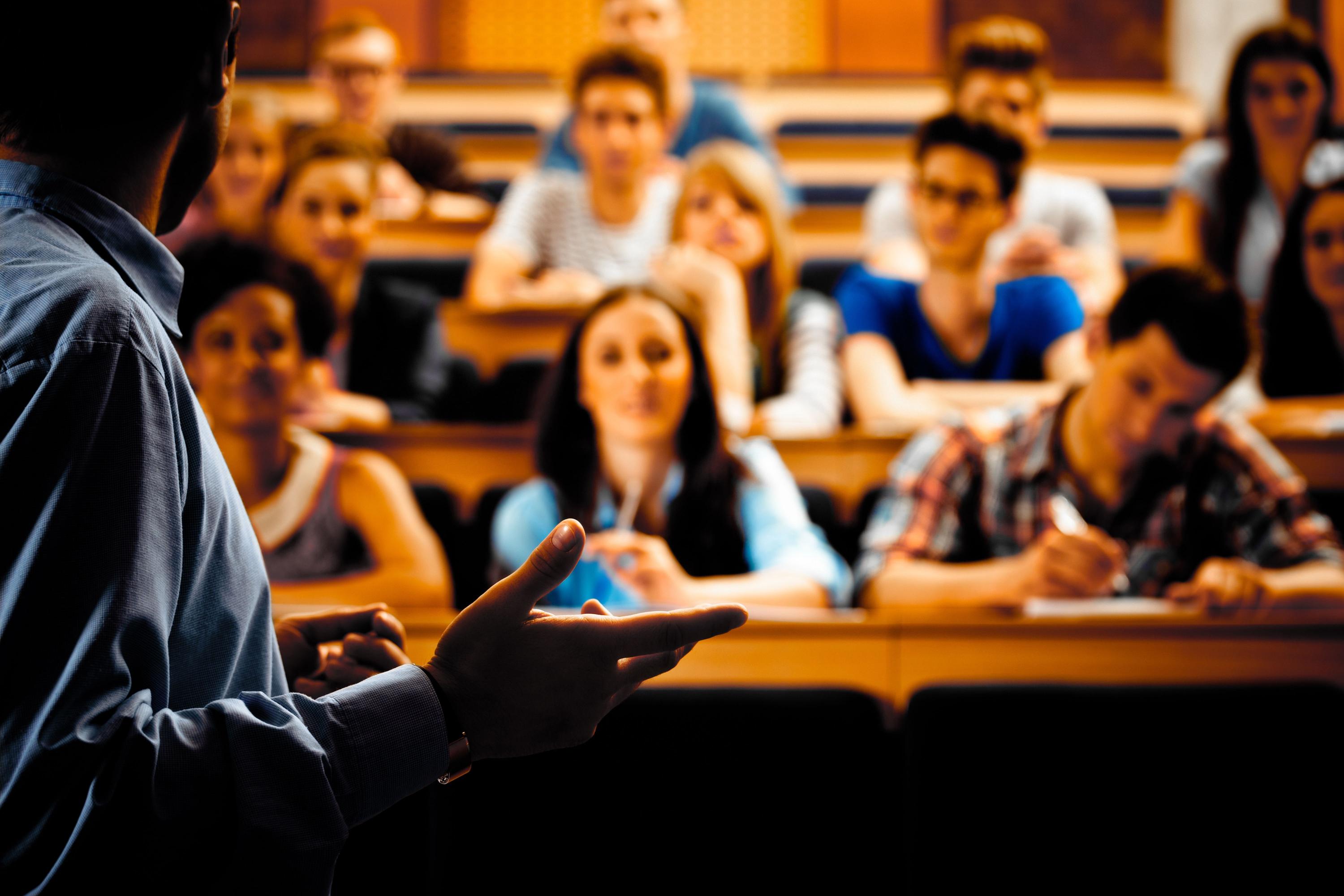 En mann holder en presentasjon for en stor gruppe studenter i en forelesningssal.