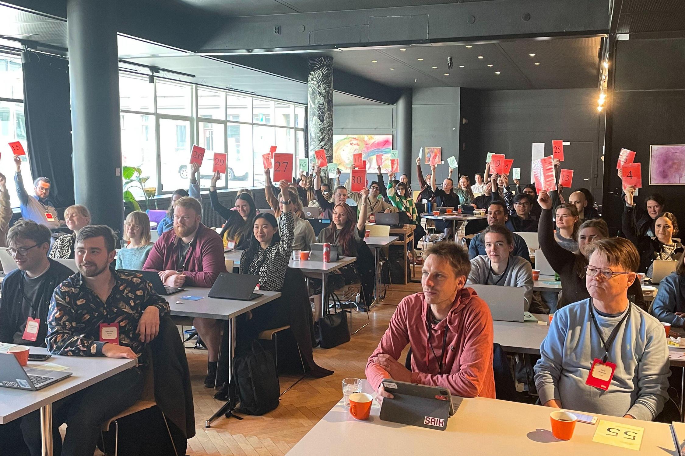 En stor gruppe mennesker holder opp et rødt ark med nummer på.