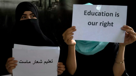 Two women protest; one in a niqab holds a sign in Persian, while another in a hijab holds a sign reading "Education is our right."